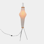 The Noguchi Araki 14A Floor Lamp by Noguchi is a tall, sculptural floor lamp inspired by Japanese craftsmanship, featuring a white ribbed shade, wooden accents, and three slender metal legs. Reminiscent of Akari Light Sculptures and the original Noguchi Araki 14A design, this plugged-in lamp is shown illuminated against a plain white background.
