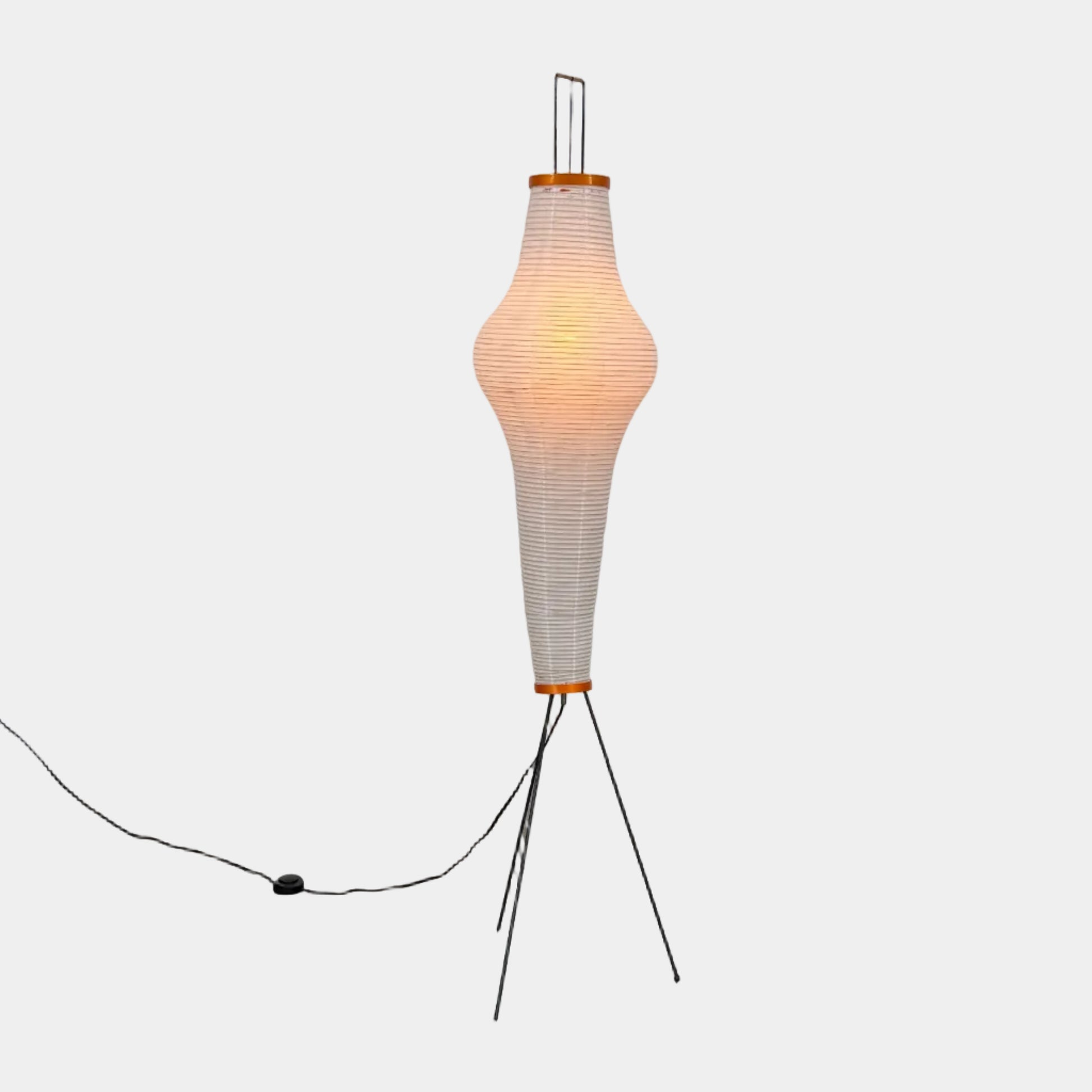 The Noguchi Araki 14A Floor Lamp by Noguchi is a tall, sculptural floor lamp inspired by Japanese craftsmanship, featuring a white ribbed shade, wooden accents, and three slender metal legs. Reminiscent of Akari Light Sculptures and the original Noguchi Araki 14A design, this plugged-in lamp is shown illuminated against a plain white background.