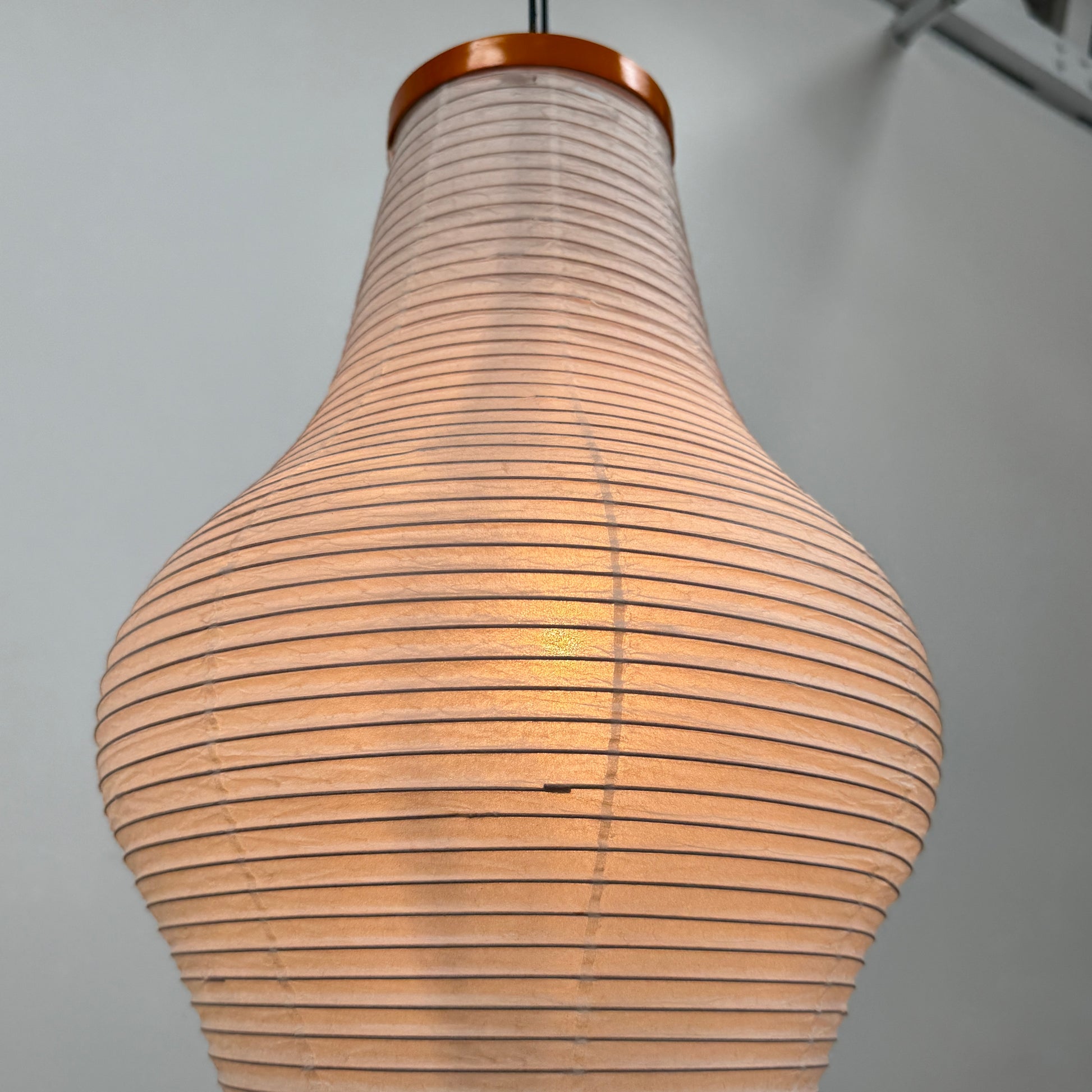 The Noguchi Araki 14A Floor Lamp by Noguchi is a tall, sculptural floor lamp inspired by Japanese craftsmanship, featuring a white ribbed shade, wooden accents, and three slender metal legs. Reminiscent of Akari Light Sculptures and the original Noguchi Araki 14A design, this plugged-in lamp is shown illuminated against a plain white background.