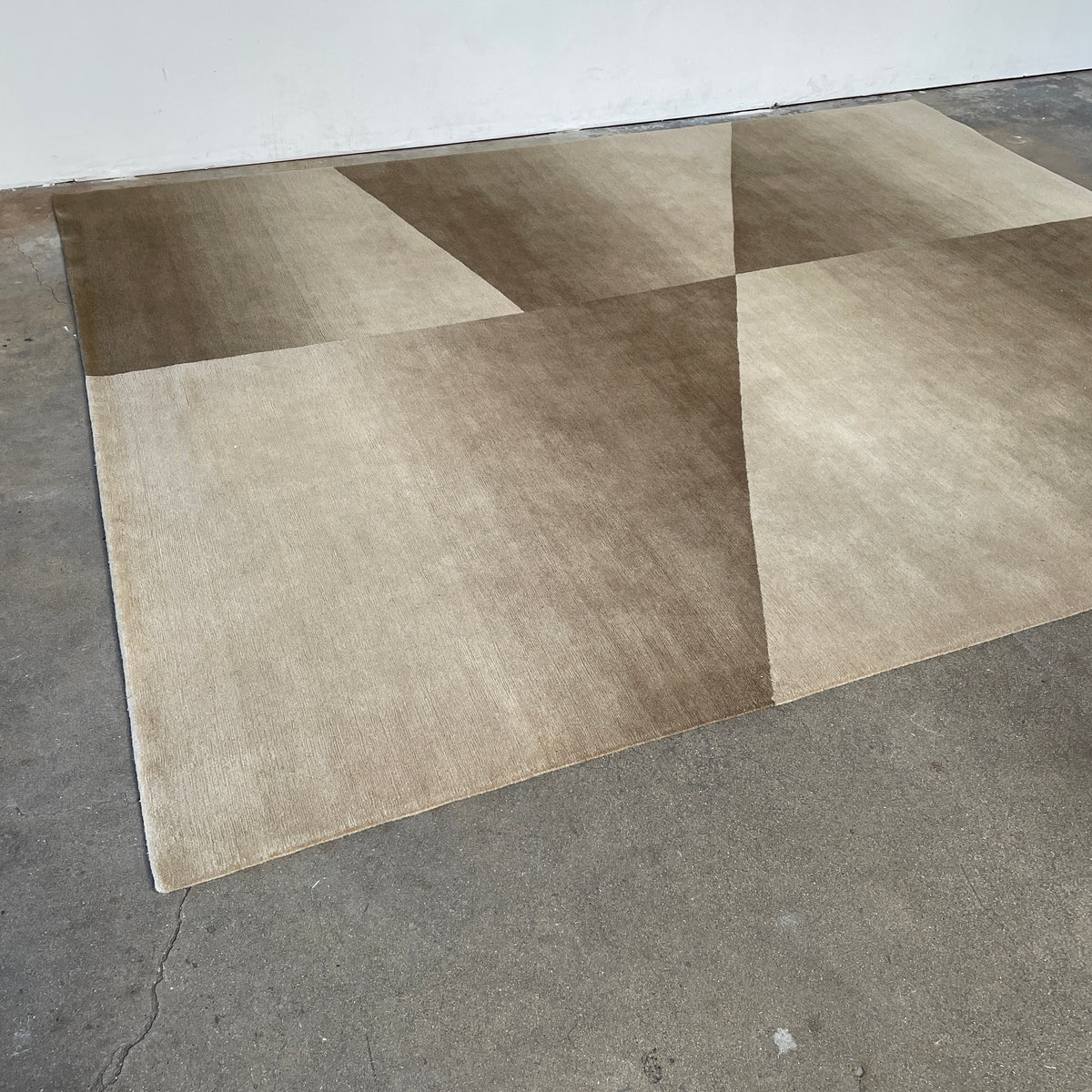 The Delinear Facet Cropped Wool Rug, offered by Delinear, is elegantly positioned on a light gray floor. It showcases modern abstract designs in beige and taupe, with diagonal lines and subtle texture.