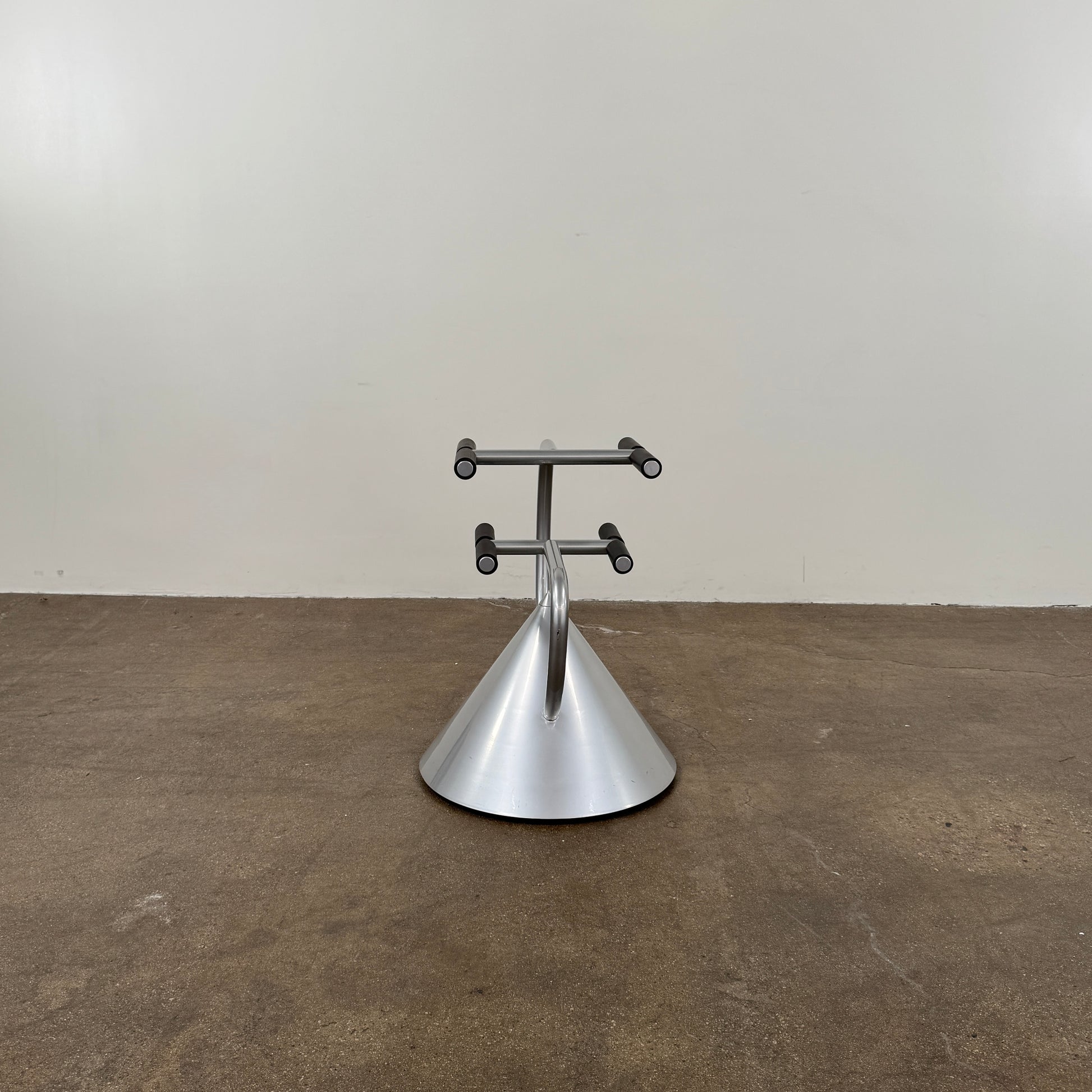 A silver metal cone base supports two curved arms with four black cylindrical grips, arranged symmetrically against a plain light background—an aesthetic reminiscent of the playful geometry seen in the Memphis movement, embodied by the Vintage Postmodern “Hotel Zeus” TV Stand for Zeus Milano by Zeus.