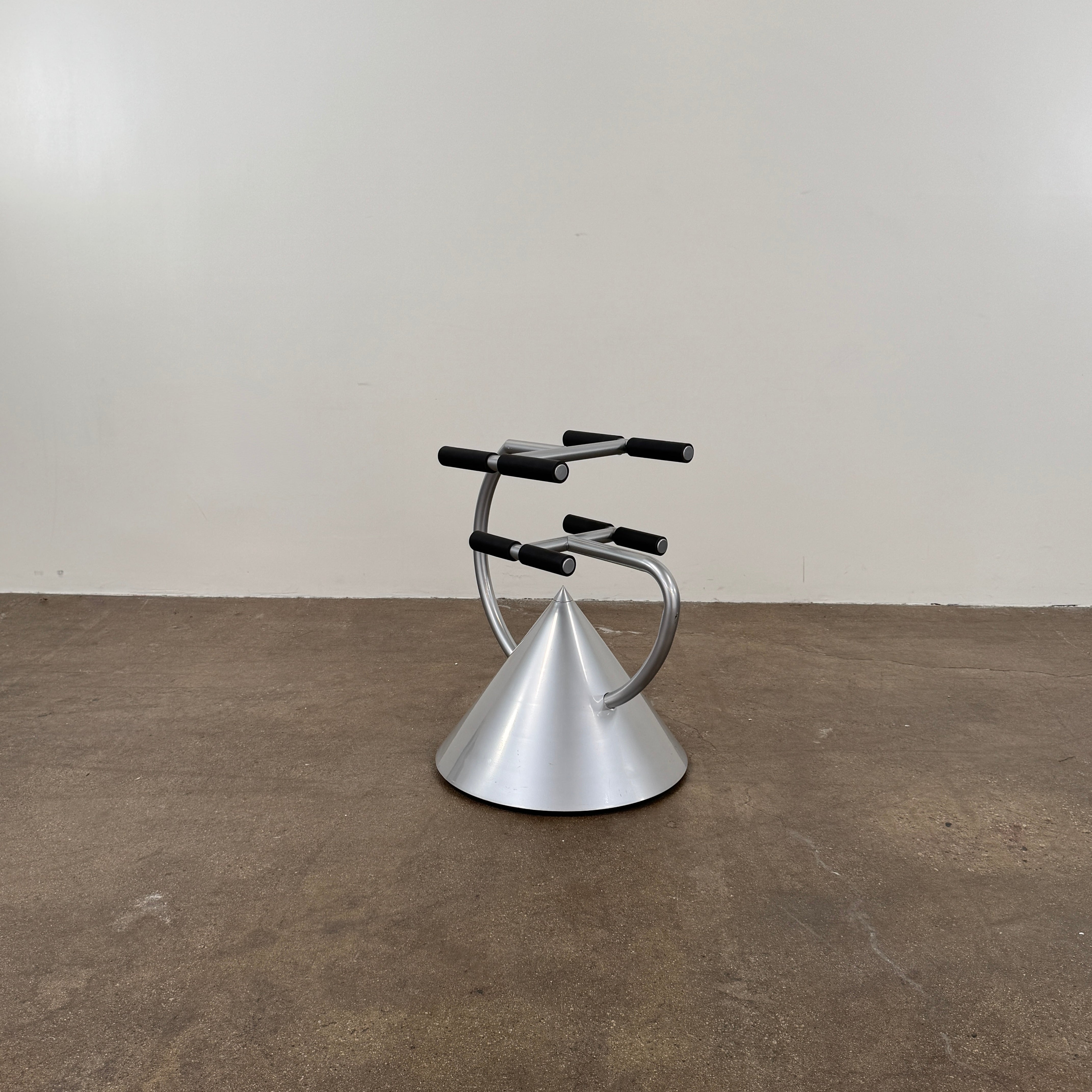 A silver metal cone base supports two curved arms with four black cylindrical grips, arranged symmetrically against a plain light background—an aesthetic reminiscent of the playful geometry seen in the Memphis movement, embodied by the Vintage Postmodern “Hotel Zeus” TV Stand for Zeus Milano by Zeus.