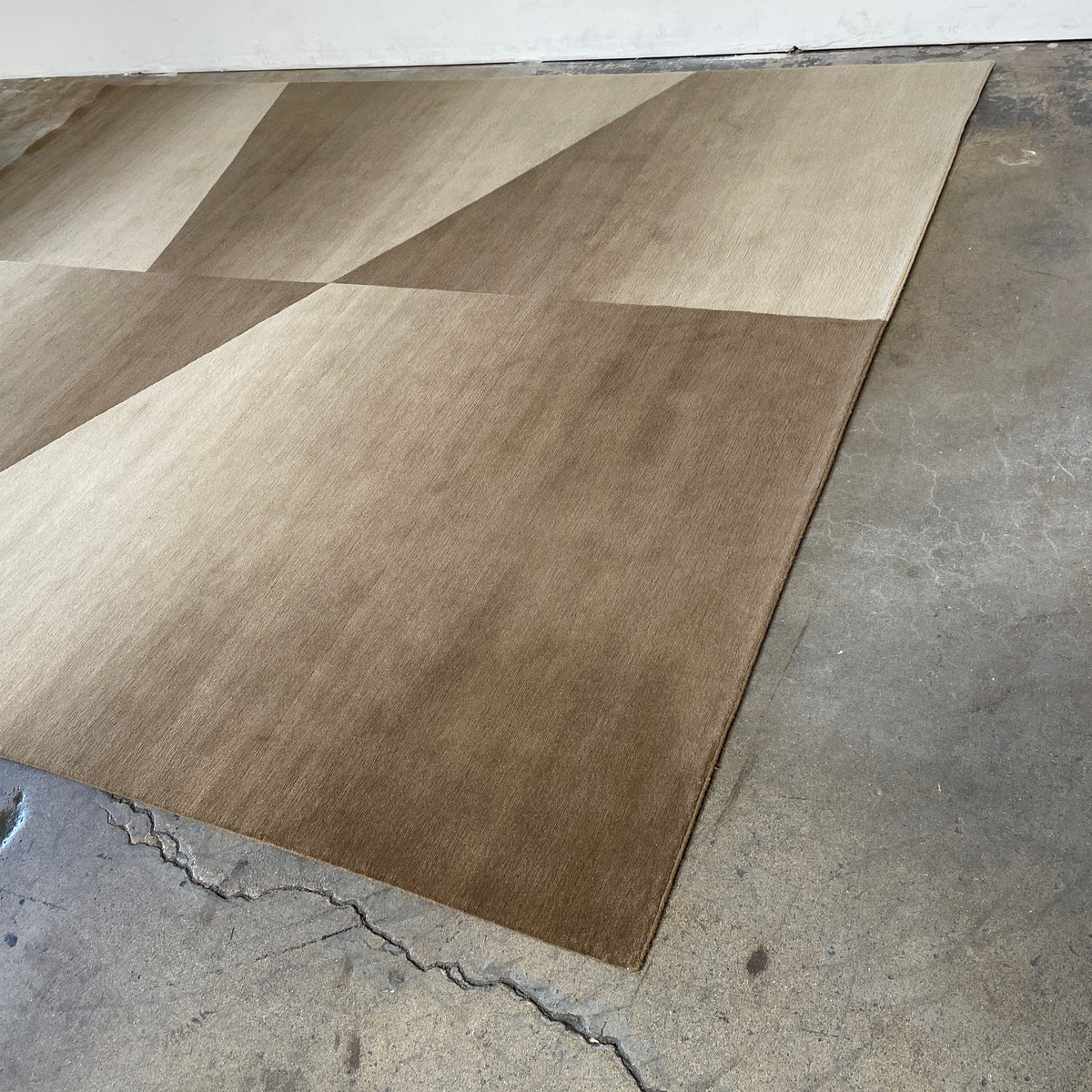 The Delinear Facet Cropped Wool Rug, offered by Delinear, is elegantly positioned on a light gray floor. It showcases modern abstract designs in beige and taupe, with diagonal lines and subtle texture.