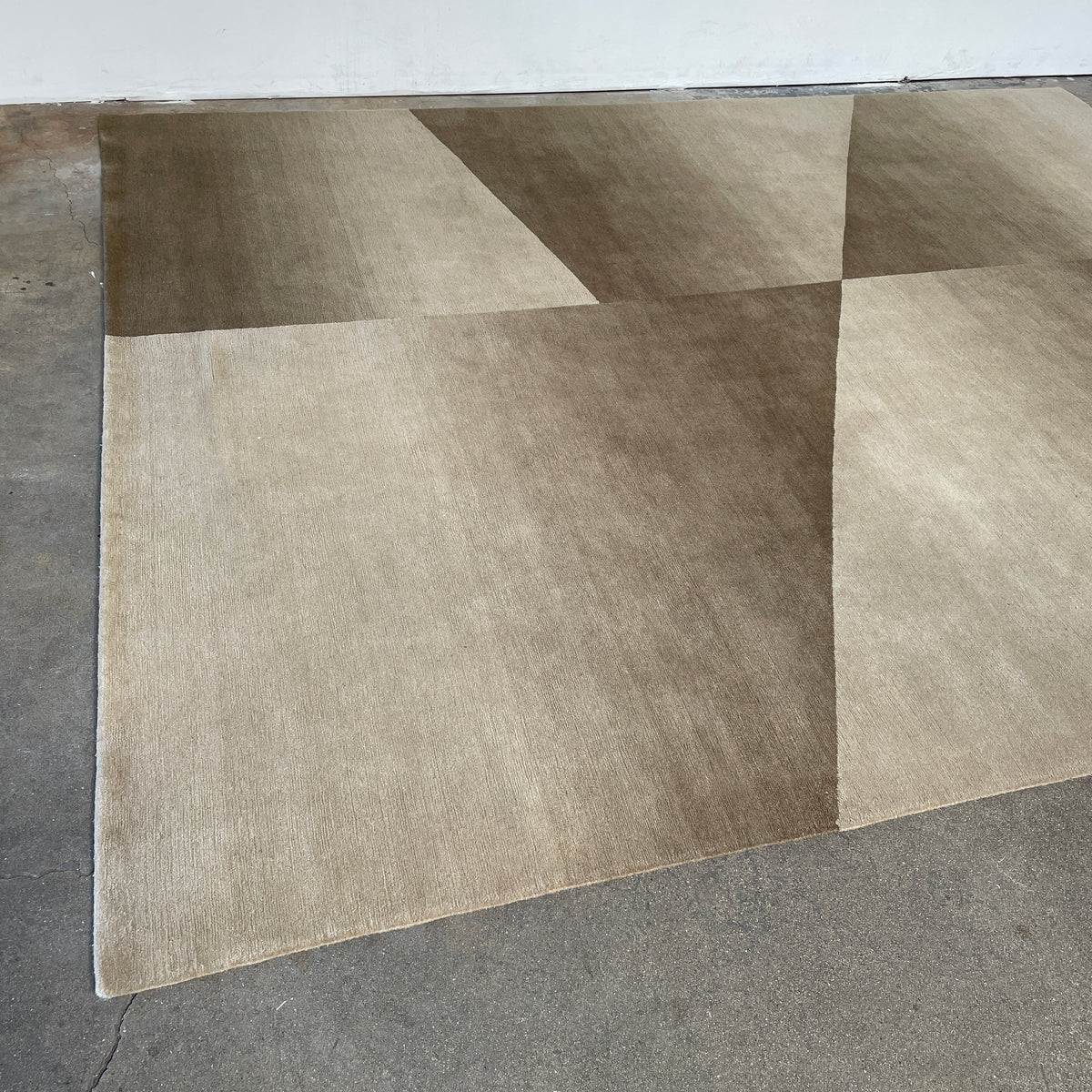 The Delinear Facet Cropped Wool Rug, offered by Delinear, is elegantly positioned on a light gray floor. It showcases modern abstract designs in beige and taupe, with diagonal lines and subtle texture.