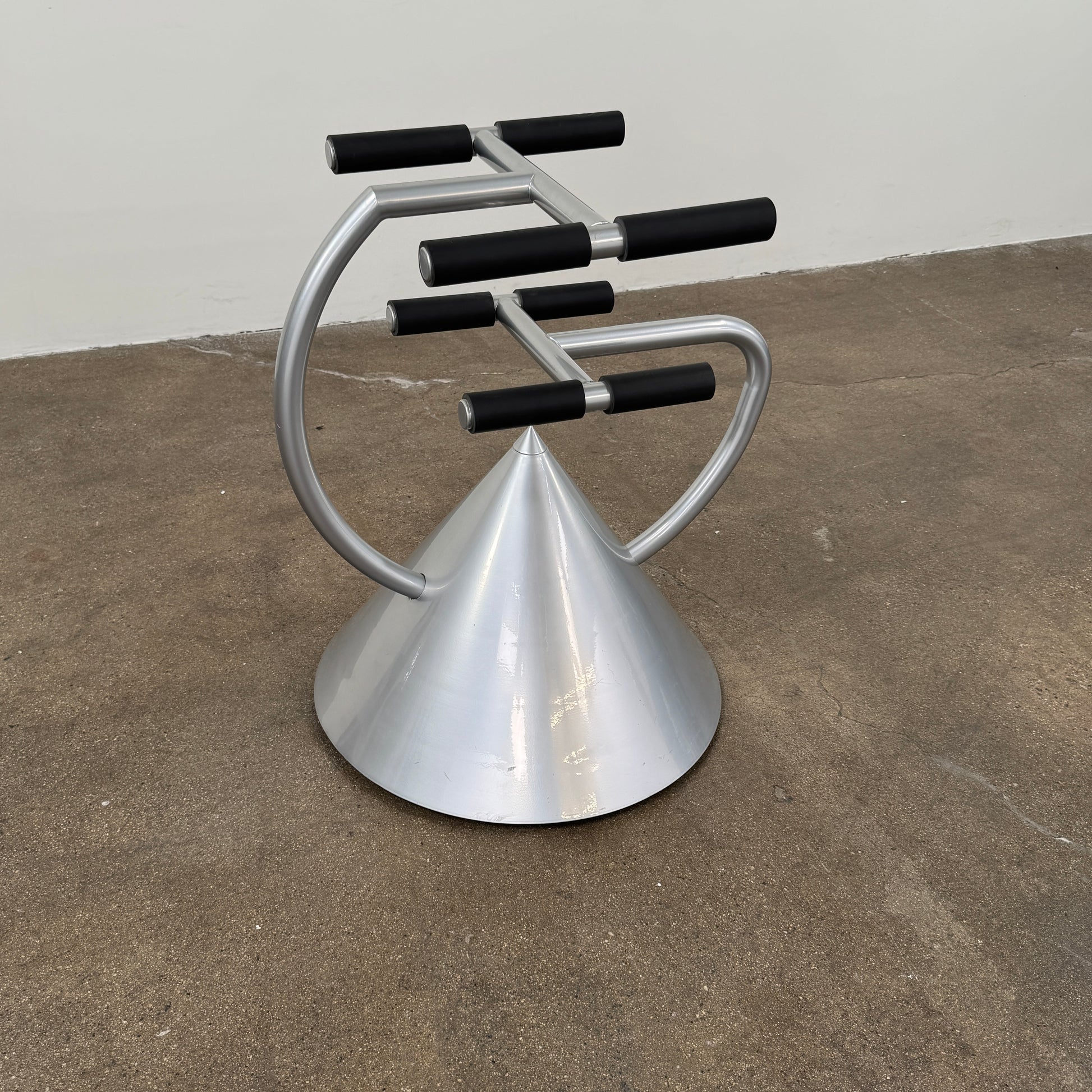 A silver metal cone base supports two curved arms with four black cylindrical grips, arranged symmetrically against a plain light background—an aesthetic reminiscent of the playful geometry seen in the Memphis movement, embodied by the Vintage Postmodern “Hotel Zeus” TV Stand for Zeus Milano by Zeus.