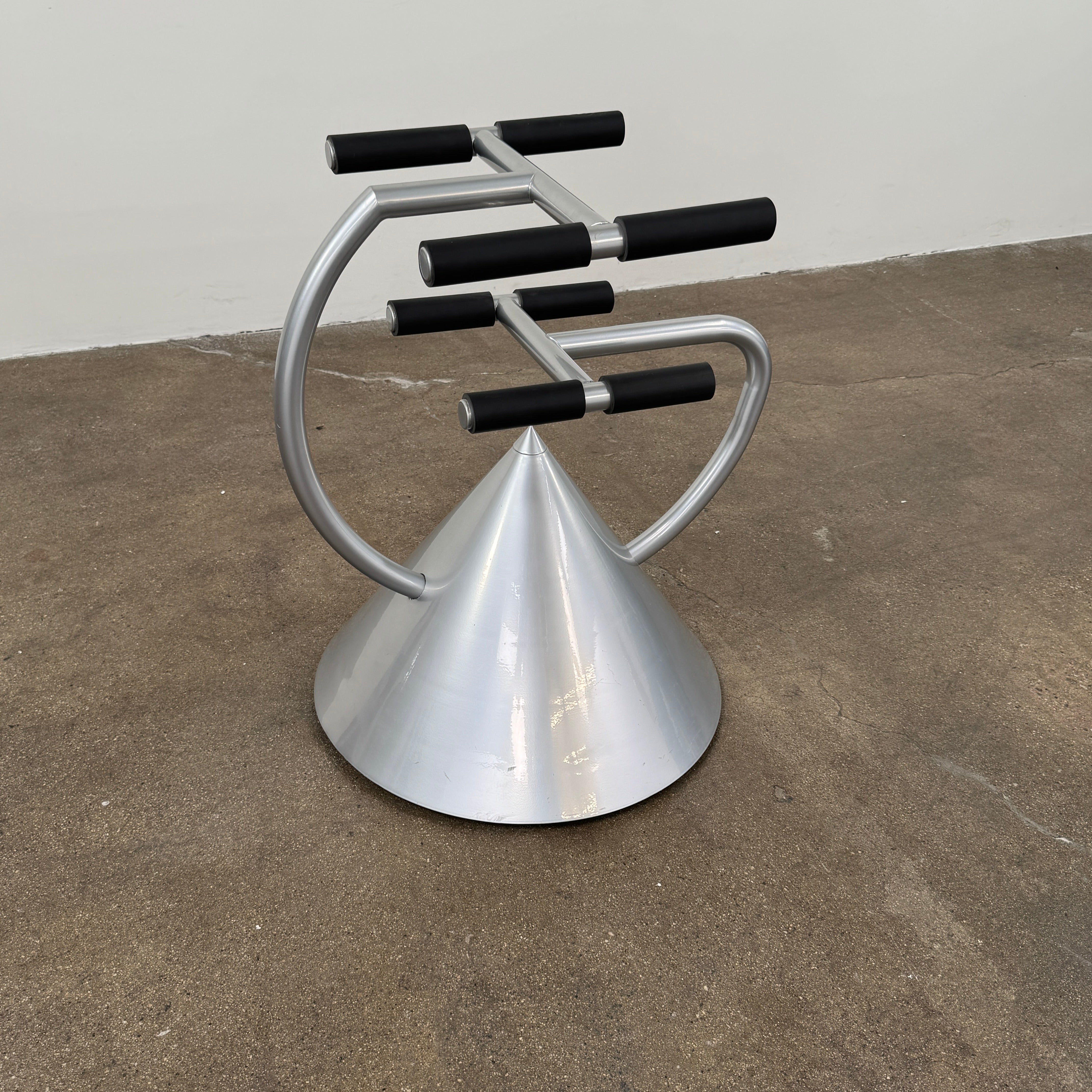 A silver metal cone base supports two curved arms with four black cylindrical grips, arranged symmetrically against a plain light background—an aesthetic reminiscent of the playful geometry seen in the Memphis movement, embodied by the Vintage Postmodern “Hotel Zeus” TV Stand for Zeus Milano by Zeus.