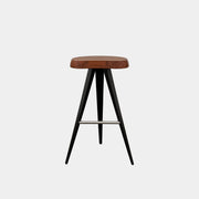 A Cassina Mexique Stool by Cassina, featuring a wooden round seat, three black angled legs, and a metal footrest, is displayed against a plain white background—highlighting its mid-century craftsmanship inspired by Charlotte Perriand.