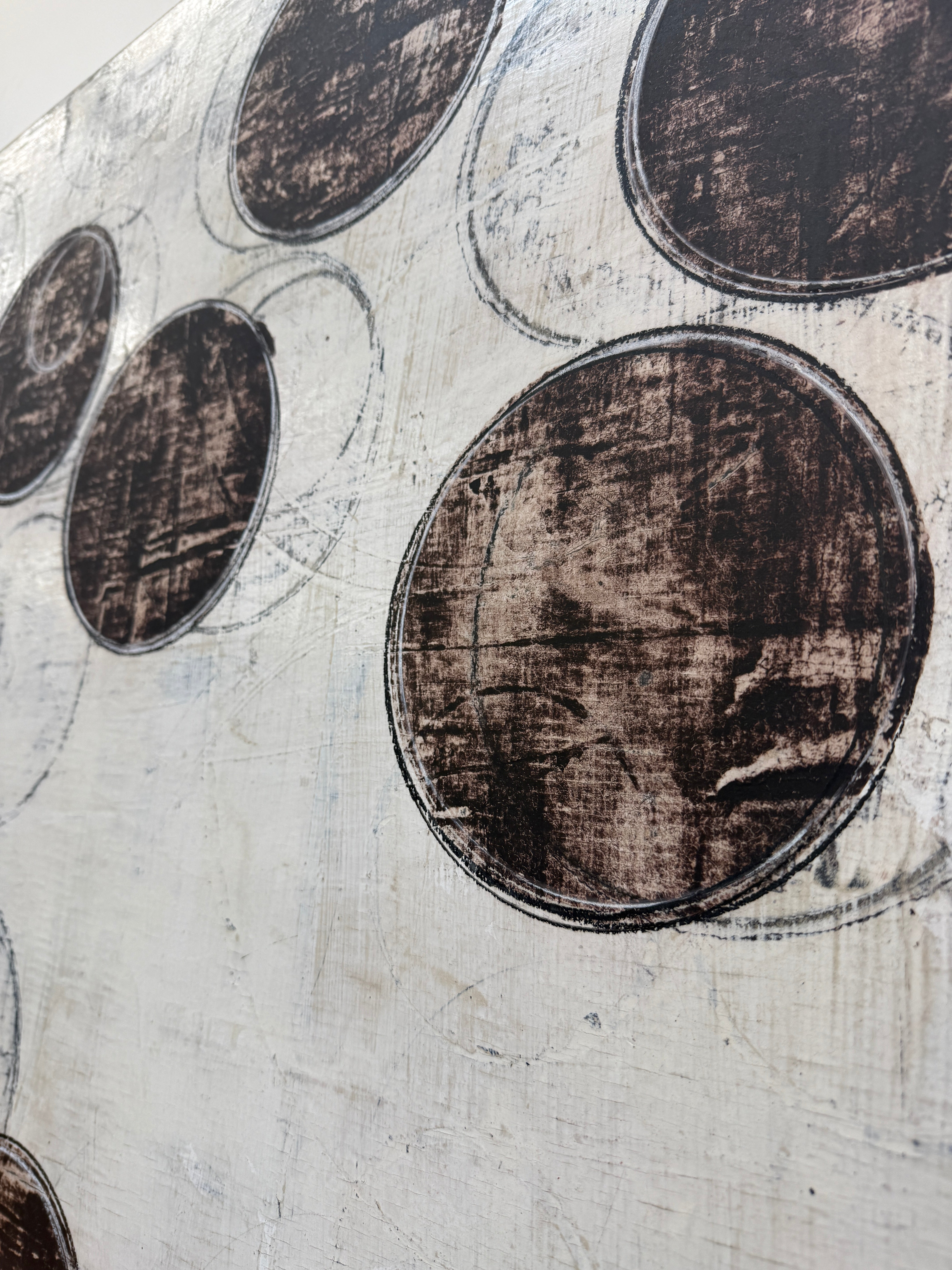 Painting: Circles by Ron Piler from Modern Resale features overlapping black and gray circles on a textured white background, displayed against a white wall on a concrete floor.