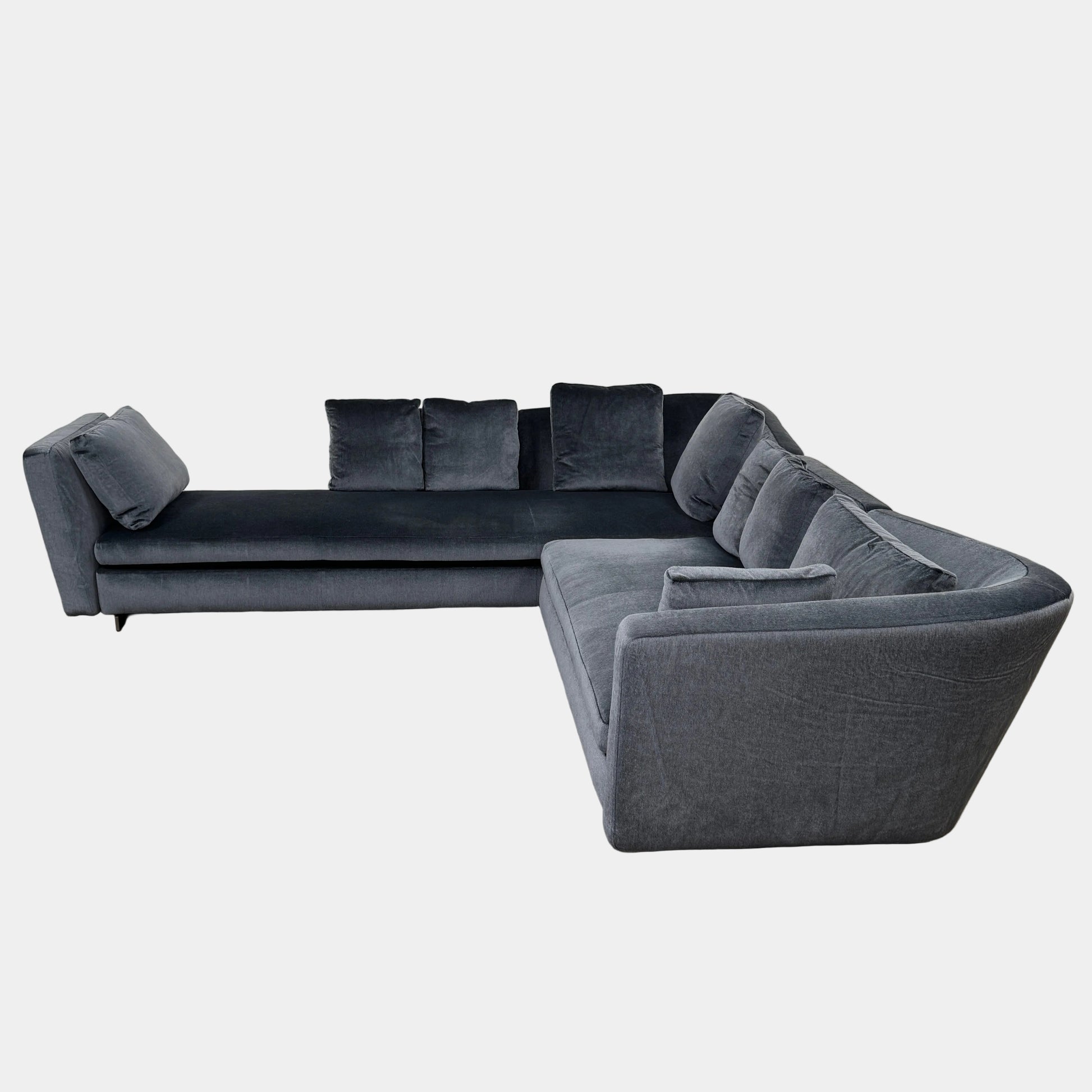 A contemporary Minotti Seymour Sofa, featuring a grey L-shaped design inspired by architectural forms, includes five matching back cushions and one side cushion, all upholstered in fabric and presented against a plain white background.