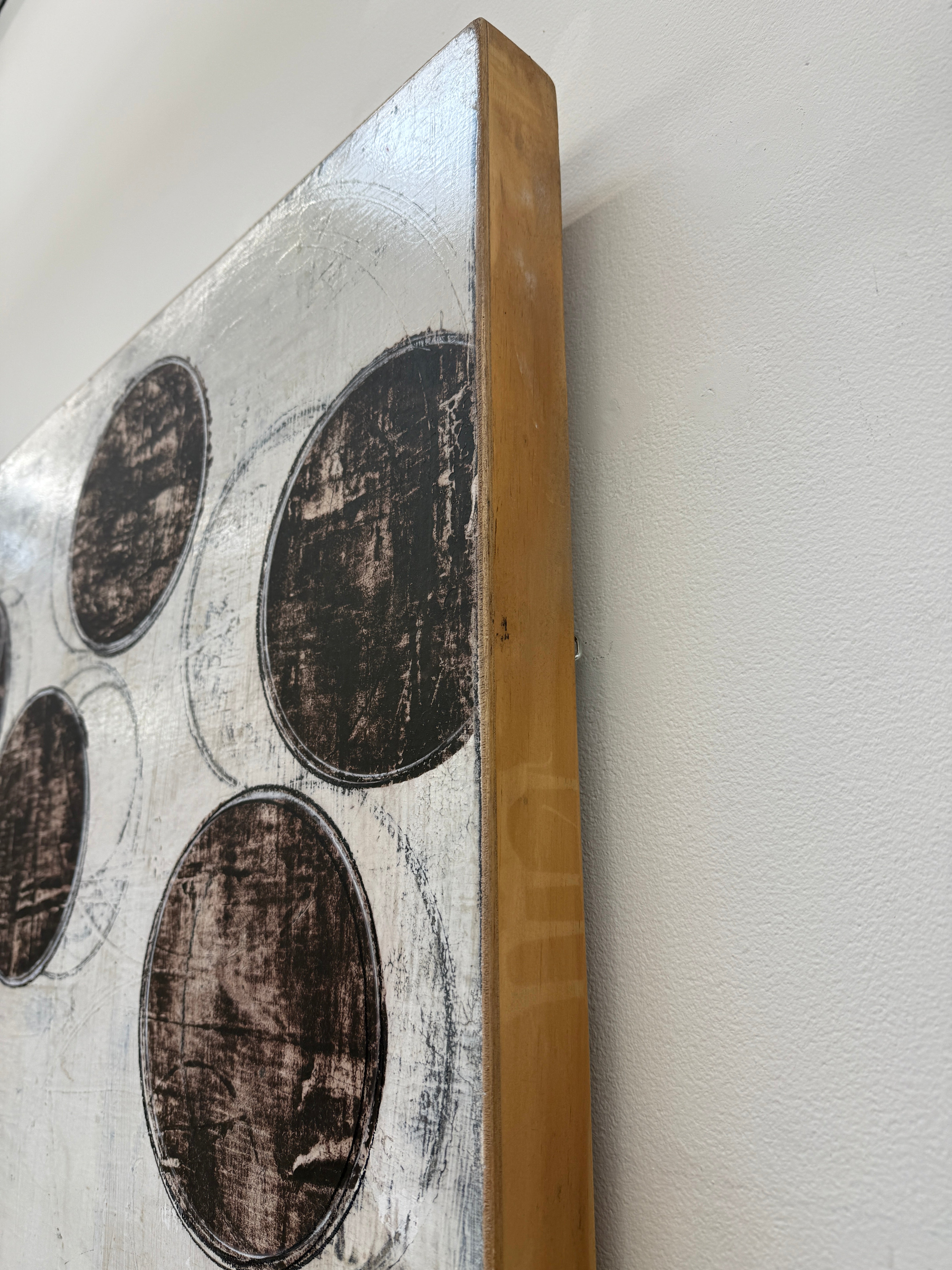 Painting: Circles by Ron Piler from Modern Resale features overlapping black and gray circles on a textured white background, displayed against a white wall on a concrete floor.
