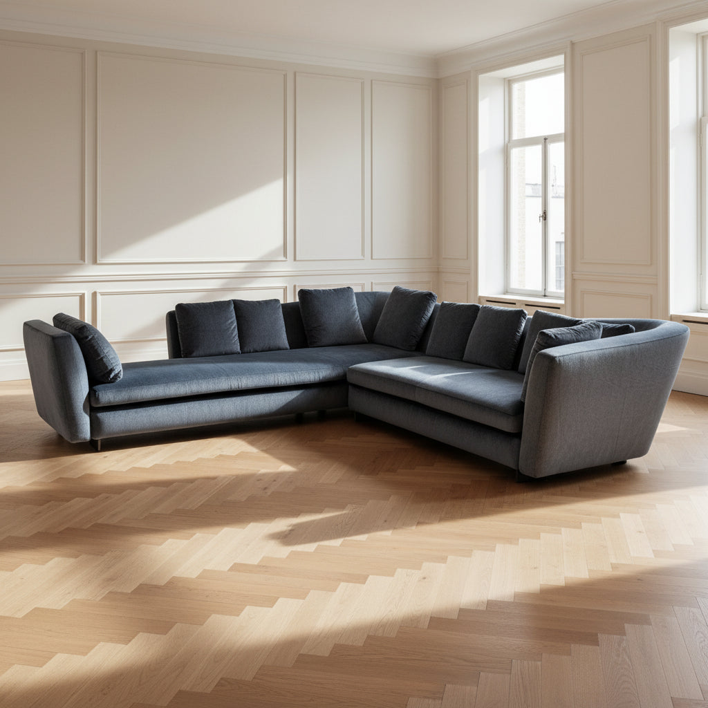 A contemporary Minotti Seymour Sofa, featuring a grey L-shaped design inspired by architectural forms, includes five matching back cushions and one side cushion, all upholstered in fabric and presented against a plain white background.