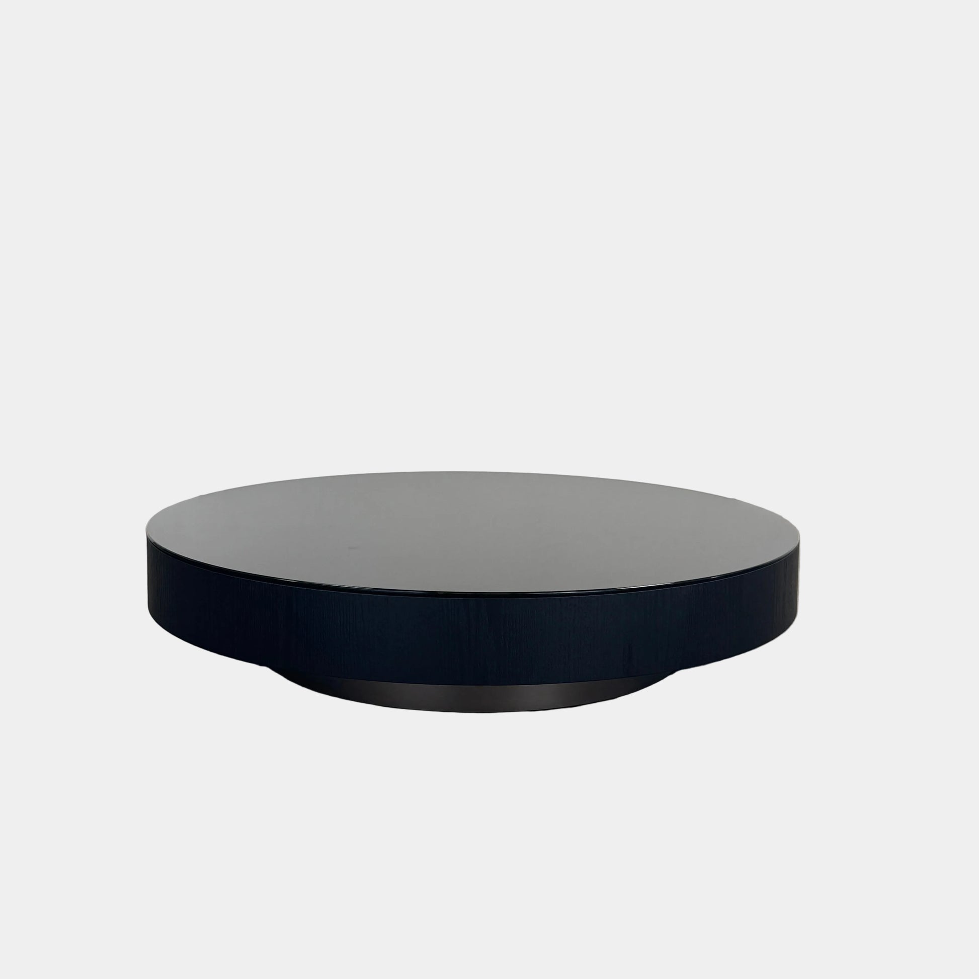 A large, round Minotti Milton Coffee Table in black rests on a polished concrete floor against a plain white wall, evoking the aesthetic of contemporary design.