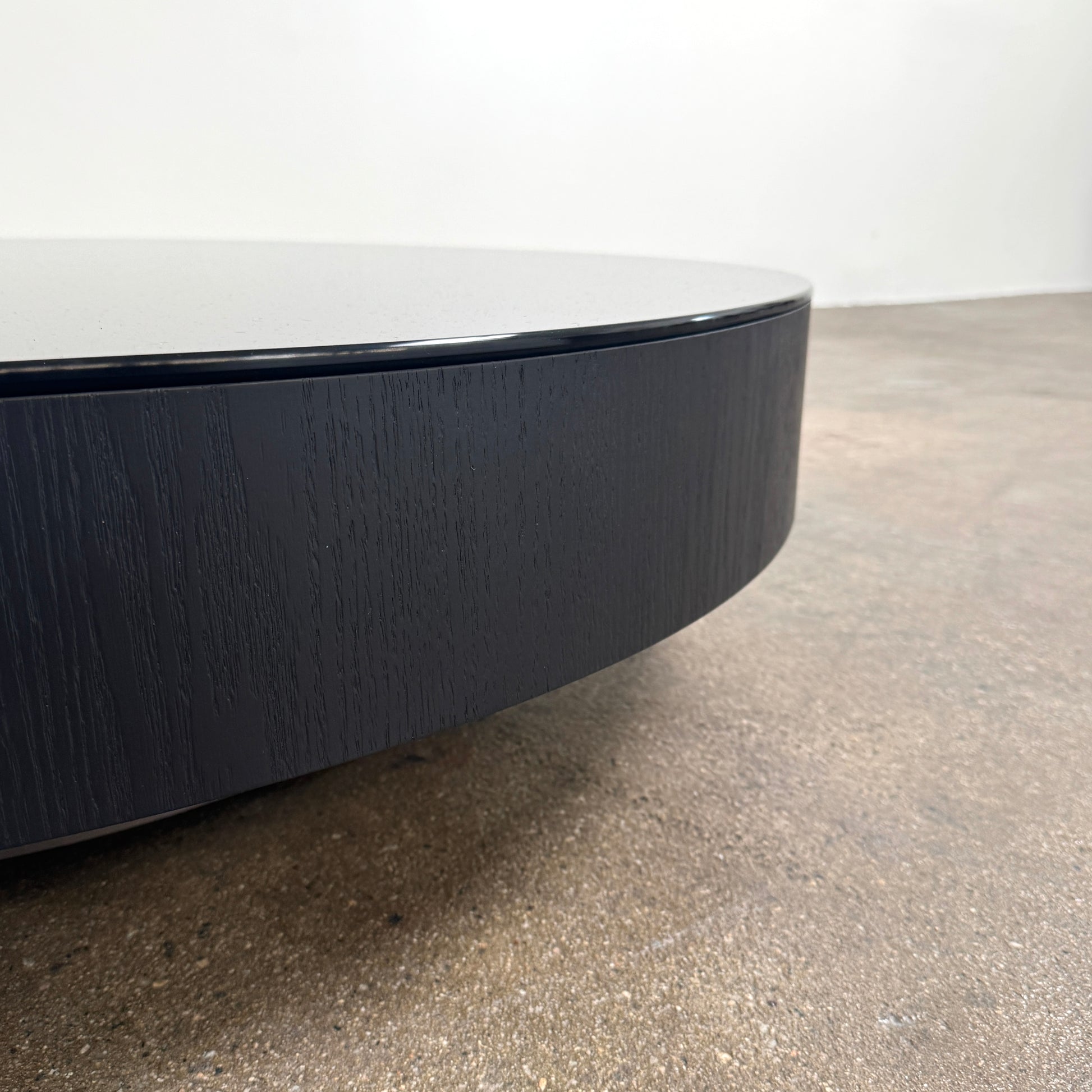 A large, round Minotti Milton Coffee Table in black rests on a polished concrete floor against a plain white wall, evoking the aesthetic of contemporary design.