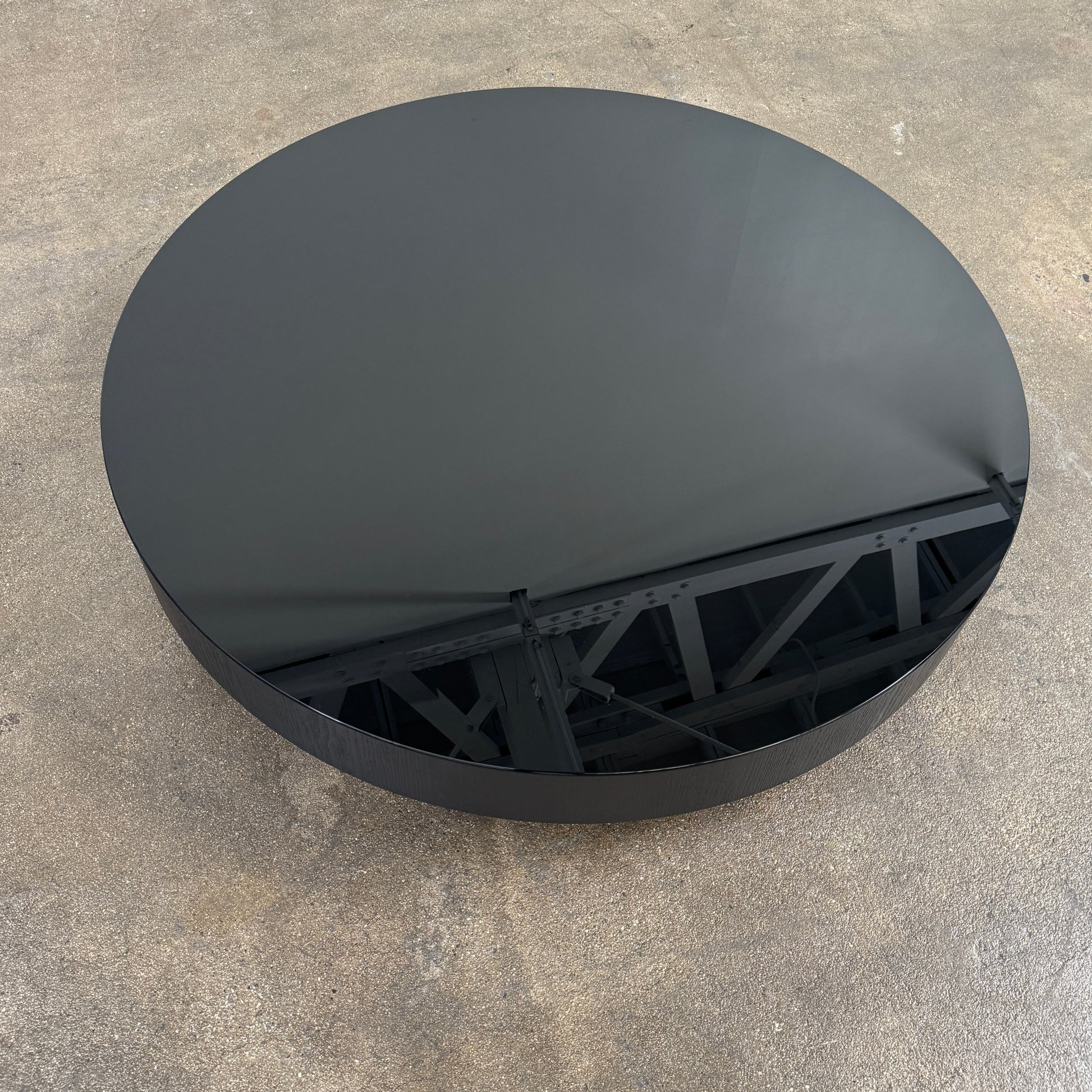 A large, round Minotti Milton Coffee Table in black rests on a polished concrete floor against a plain white wall, evoking the aesthetic of contemporary design.