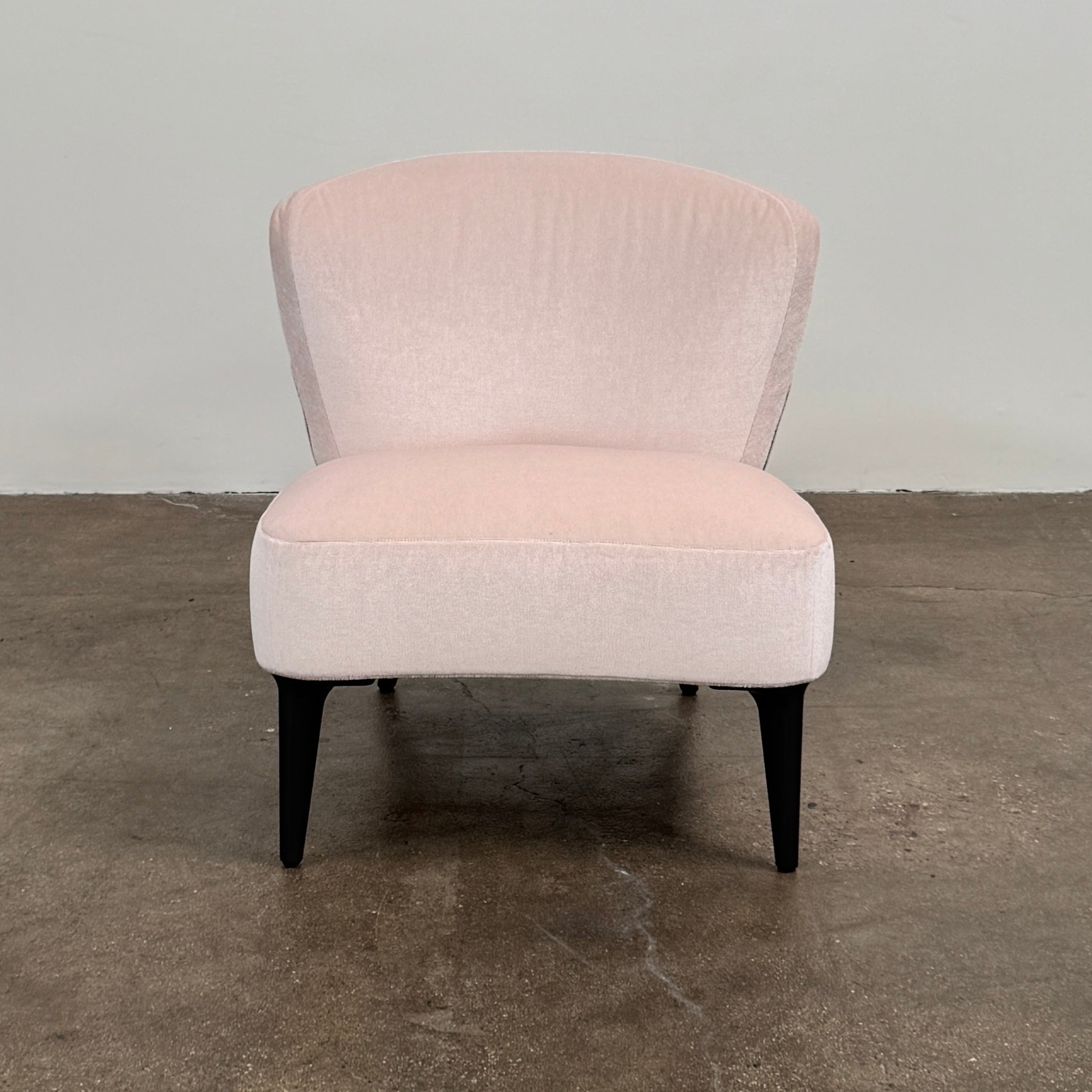 The Minotti Aston “Armchair” by Minotti features modern luxury with light pink upholstery and black wooden legs, showcased against a plain white background.