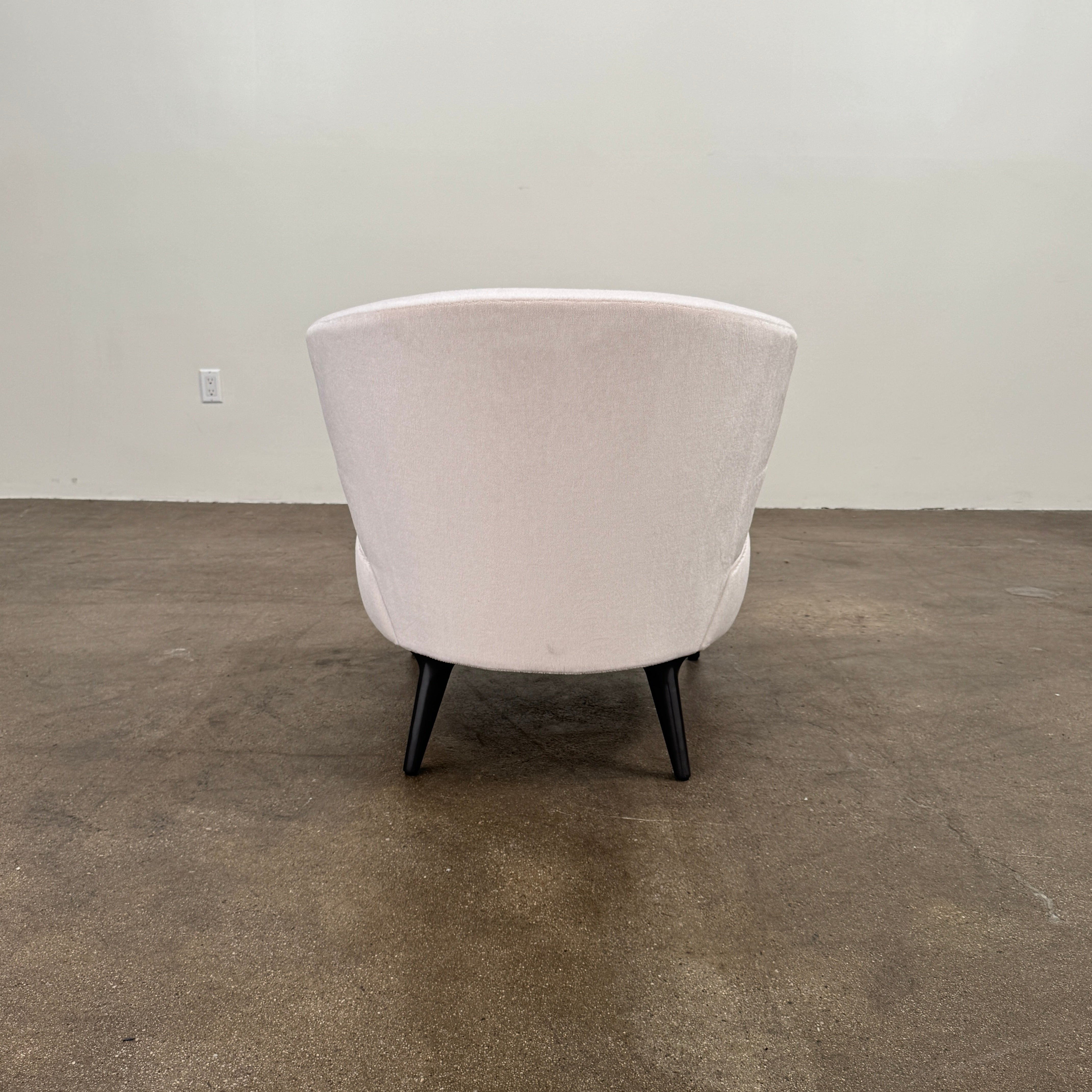 The Minotti Aston “Armchair” by Minotti features modern luxury with light pink upholstery and black wooden legs, showcased against a plain white background.