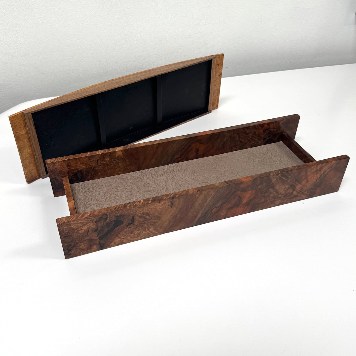 The MIke Fair Table Top Storage Box by Mike Fair Custom Furnishings features a rectangular design with raised sides and a glossy finish, highlighting the natural camphor burl and claro walnut wood grain. It is displayed on a white surface.