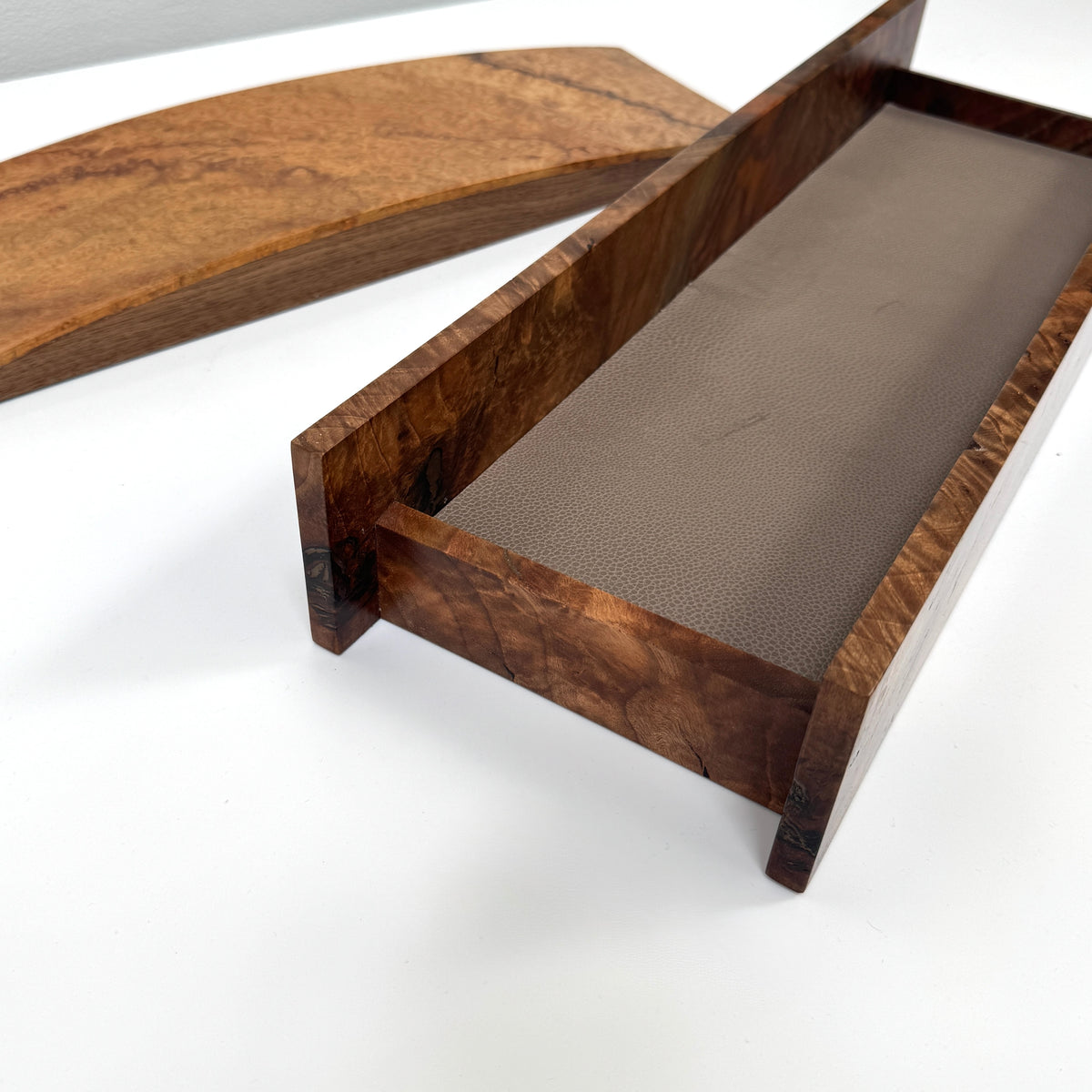 The MIke Fair Table Top Storage Box by Mike Fair Custom Furnishings features a rectangular design with raised sides and a glossy finish, highlighting the natural camphor burl and claro walnut wood grain. It is displayed on a white surface.