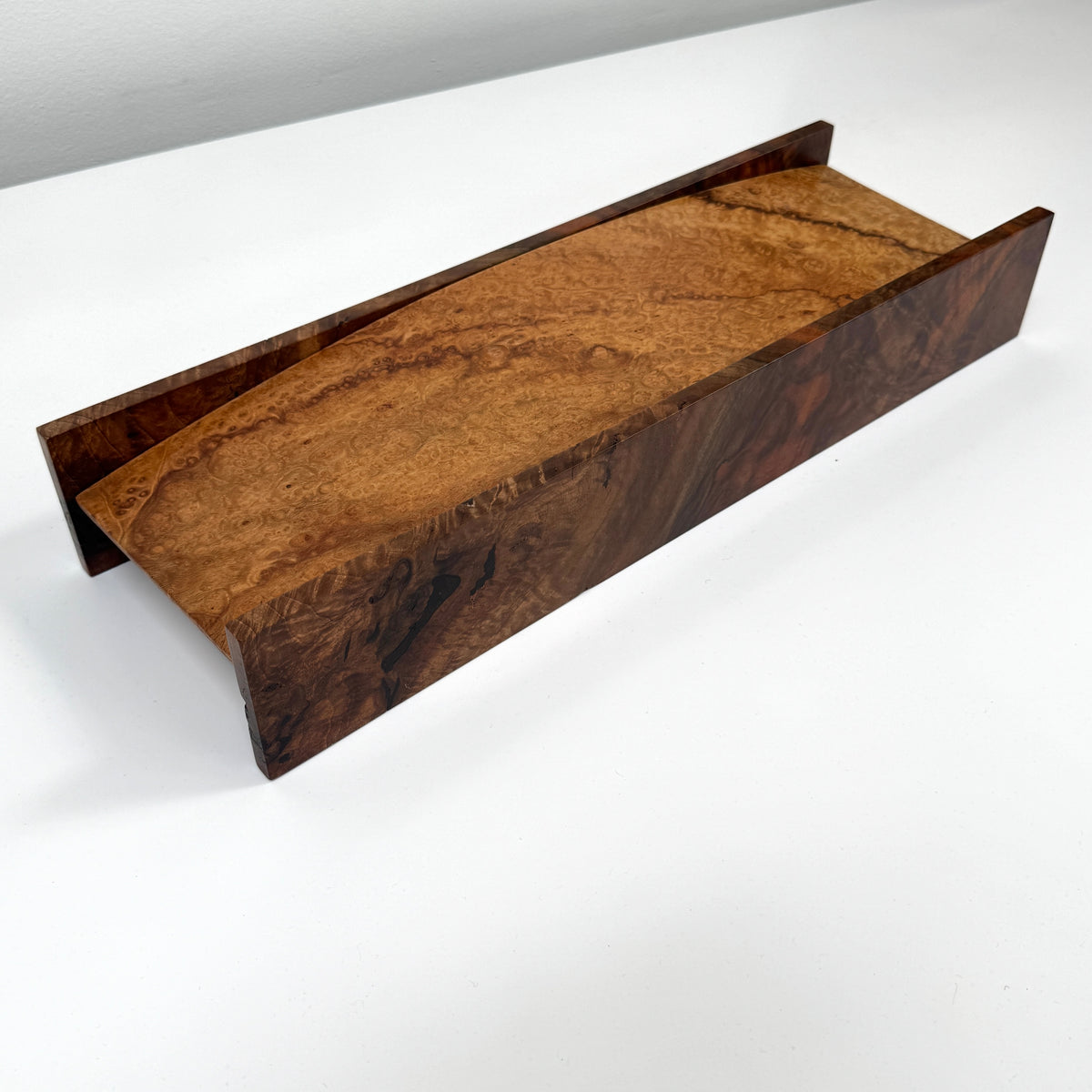 The MIke Fair Table Top Storage Box by Mike Fair Custom Furnishings features a rectangular design with raised sides and a glossy finish, highlighting the natural camphor burl and claro walnut wood grain. It is displayed on a white surface.