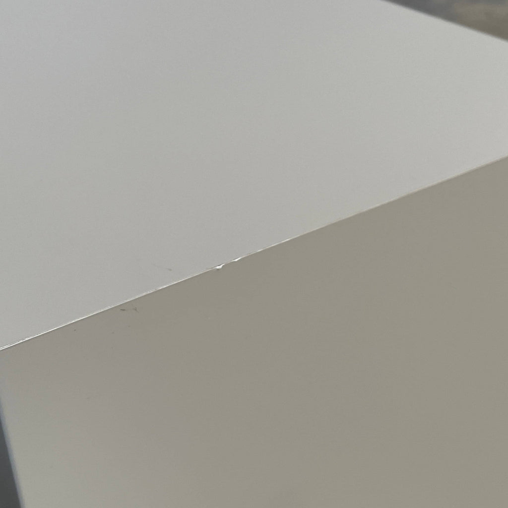 A sleek white Ligne Roset Cineline Bedside Table with a glass top.