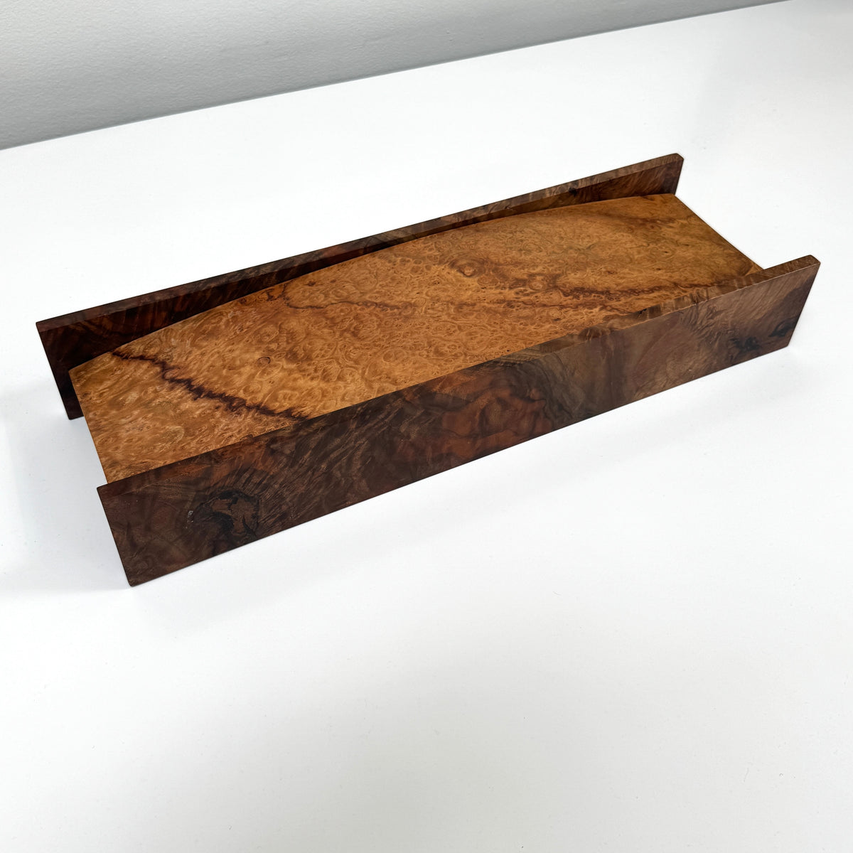 The MIke Fair Table Top Storage Box by Mike Fair Custom Furnishings features a rectangular design with raised sides and a glossy finish, highlighting the natural camphor burl and claro walnut wood grain. It is displayed on a white surface.