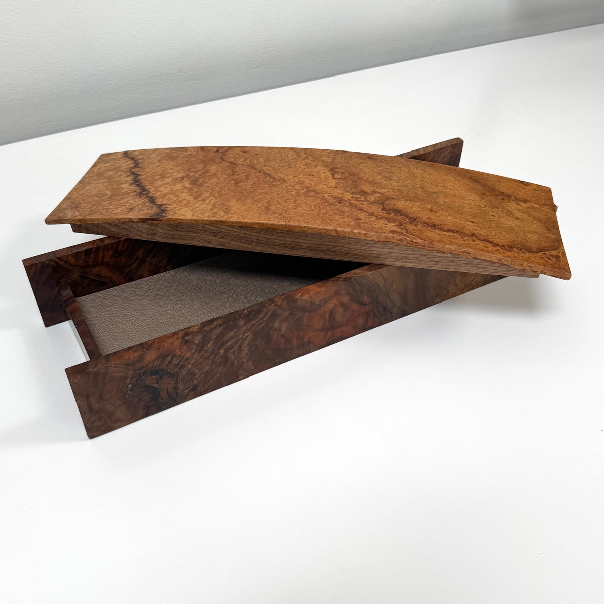 The MIke Fair Table Top Storage Box by Mike Fair Custom Furnishings features a rectangular design with raised sides and a glossy finish, highlighting the natural camphor burl and claro walnut wood grain. It is displayed on a white surface.