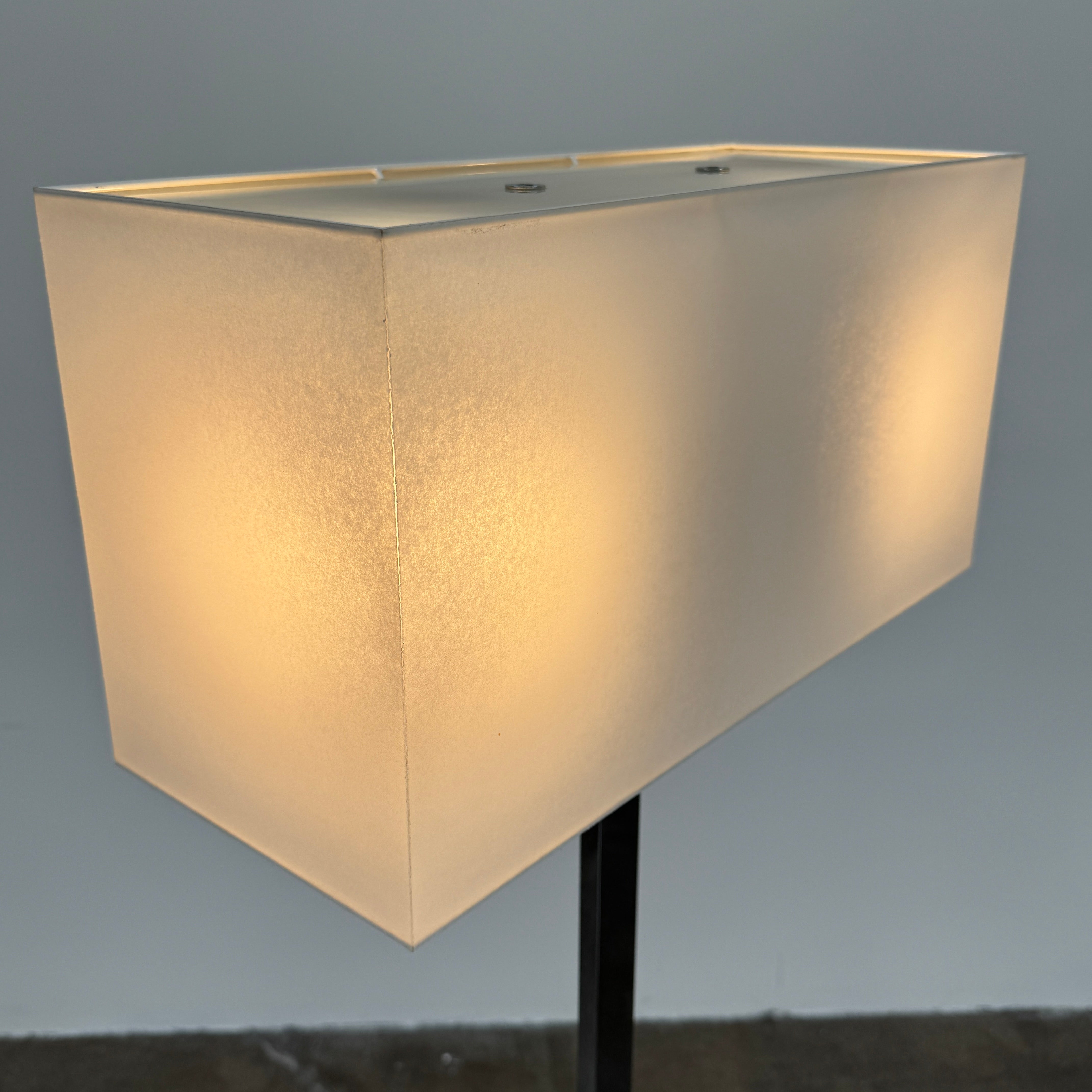 The Maxalto Leukon Floor Lamp by Maxalto features a tall chrome stand, rectangular white shade, distinctive cross-shaped base, and a black power cord with foot switch, set against a plain background.