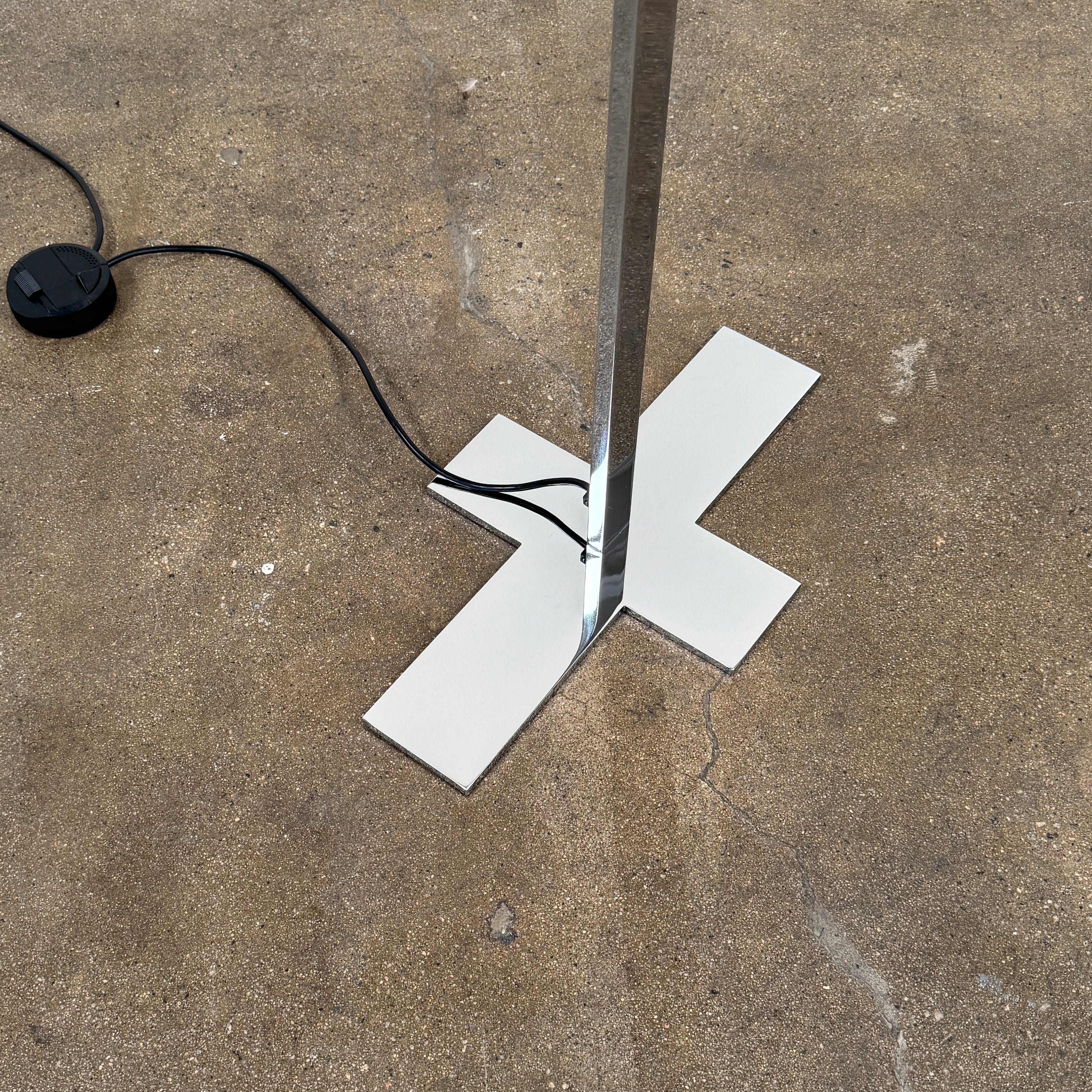 The Maxalto Leukon Floor Lamp by Maxalto features a tall chrome stand, rectangular white shade, distinctive cross-shaped base, and a black power cord with foot switch, set against a plain background.