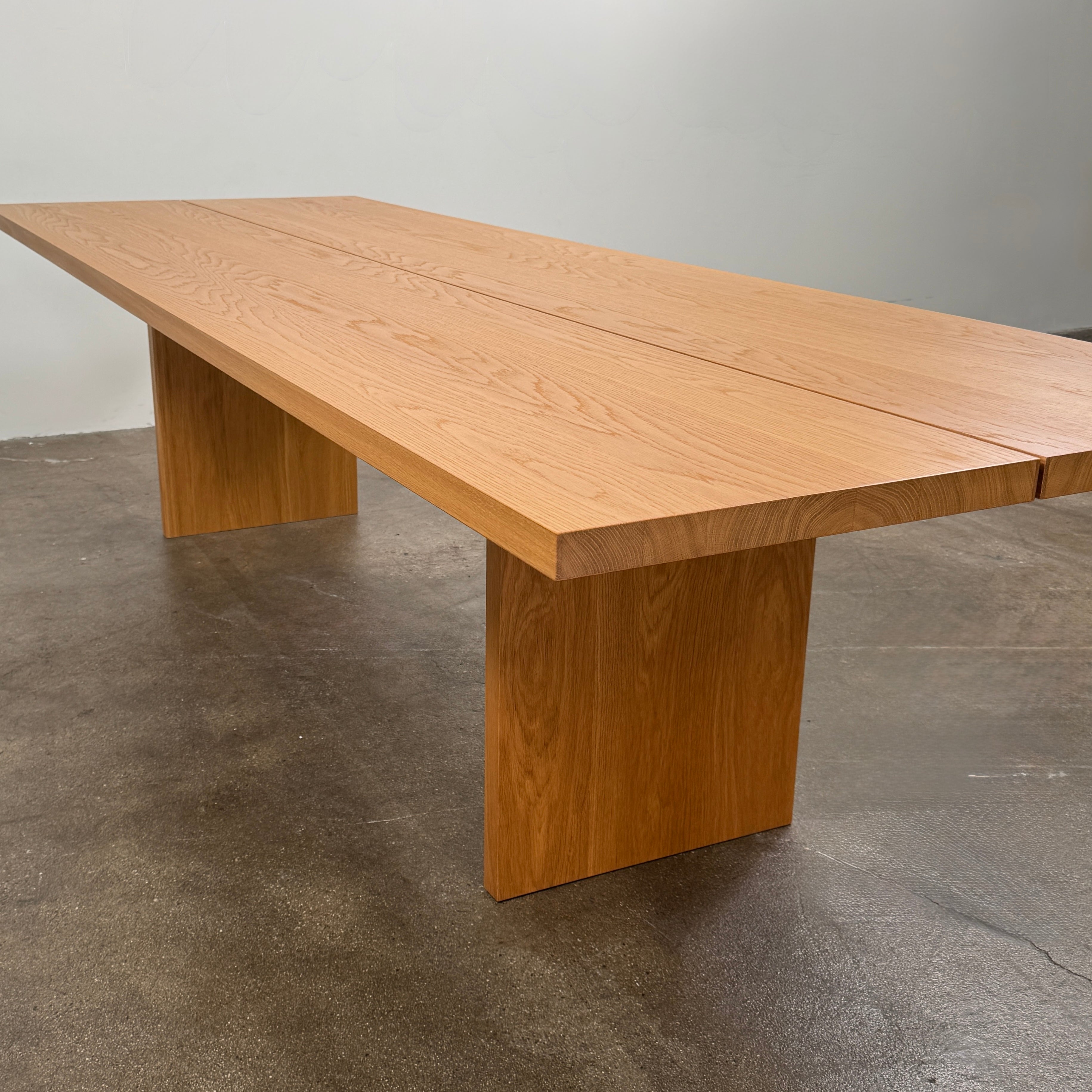 A Dk3 Gather table, crafted from solid oak with a flat rectangular top and two wide, flat legs at each end, is set against a plain white background.