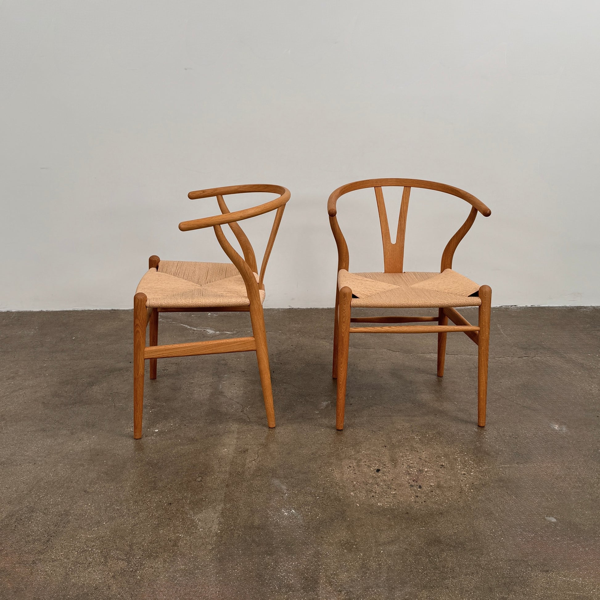 A set of two Carl Hansen & Søn Wishbone Dining Chairs by Carl Hansen & Son, featuring curved backrests and woven seats, are displayed side by side against a plain white background to highlight the renowned Danish craftsmanship inspired by Hans Wegner’s iconic design.