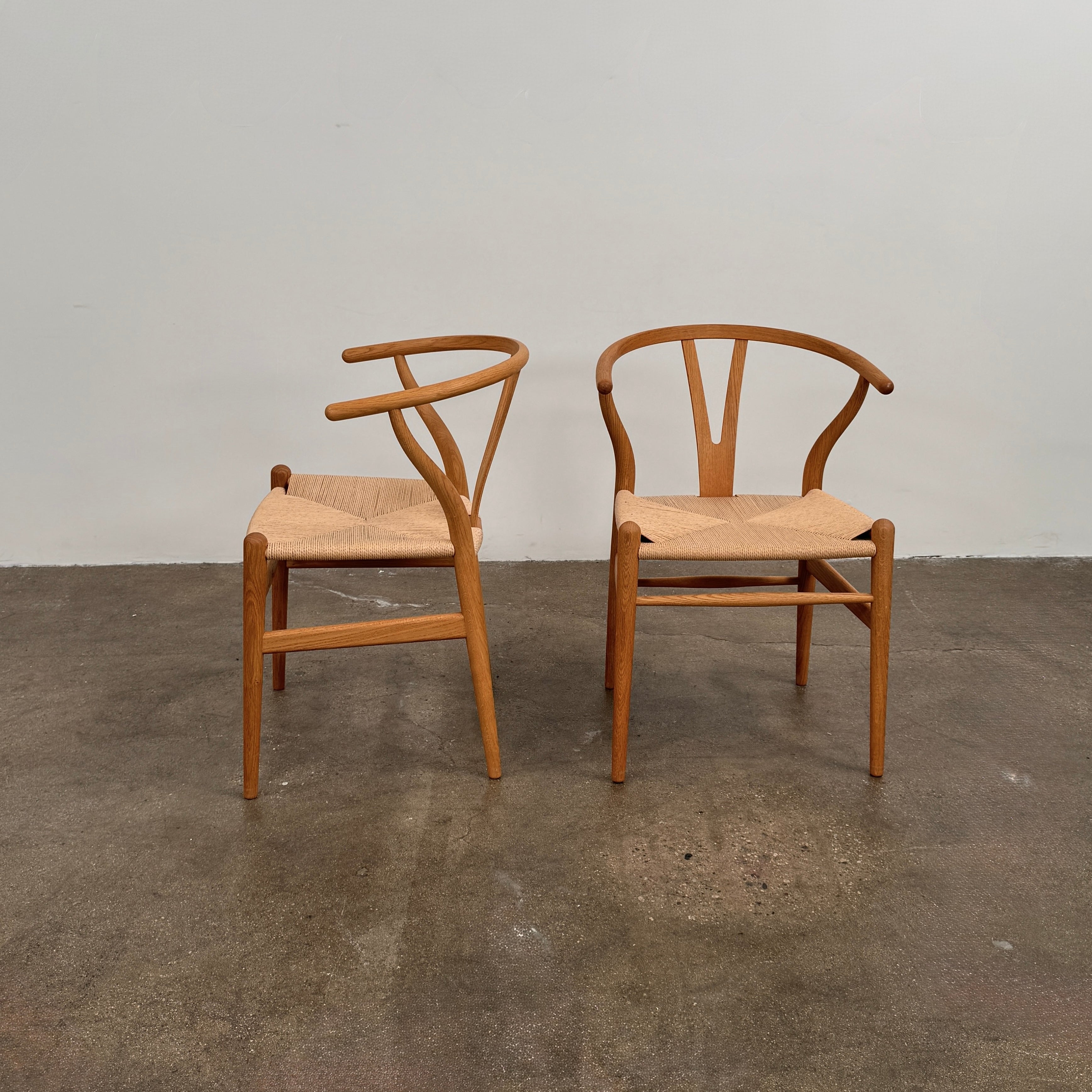 A set of two Carl Hansen & Søn Wishbone Dining Chairs by Carl Hansen & Son, featuring curved backrests and woven seats, are displayed side by side against a plain white background to highlight the renowned Danish craftsmanship inspired by Hans Wegner’s iconic design.