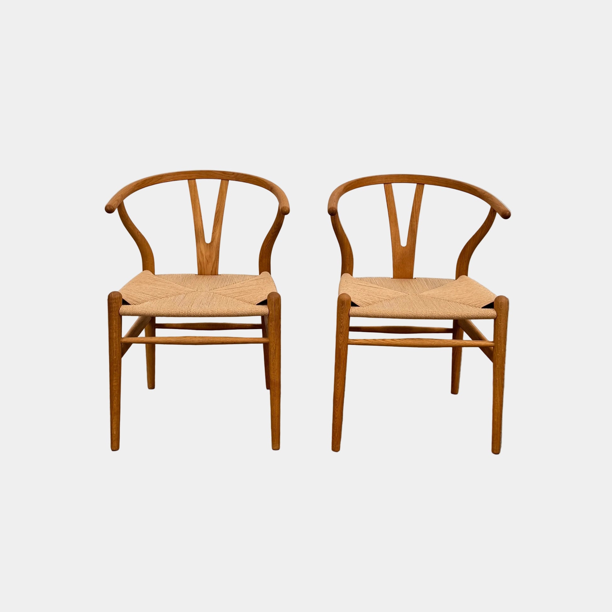 A set of two Carl Hansen & Søn Wishbone Dining Chairs by Carl Hansen & Son, featuring curved backrests and woven seats, are displayed side by side against a plain white background to highlight the renowned Danish craftsmanship inspired by Hans Wegner’s iconic design.