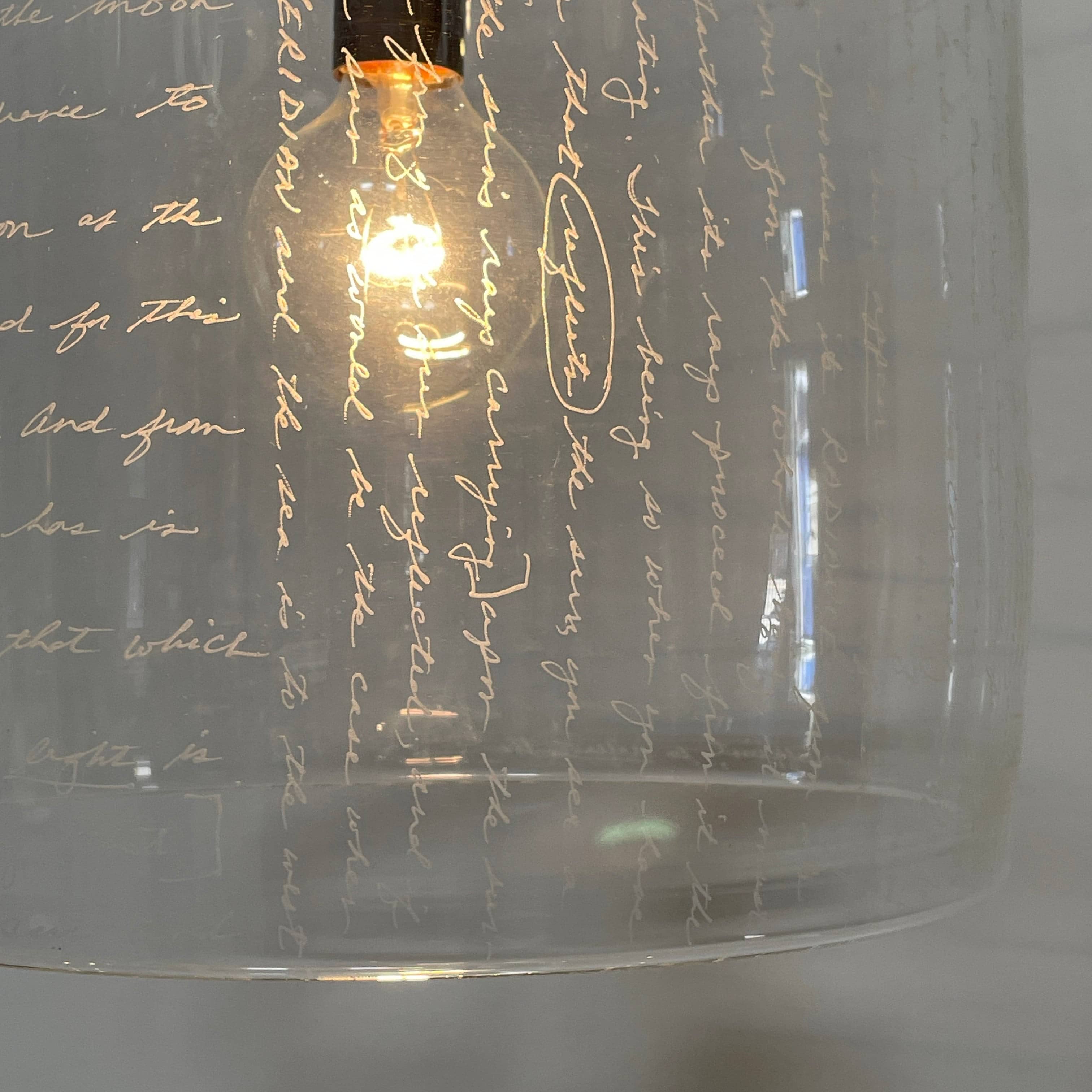 A unique functional art piece, this Alison Berger Word Pendant by Alison Berger showcases visible wires and mounting hardware against a white textured ceiling, reminiscent of Alison Berger's Word Pendant designs.