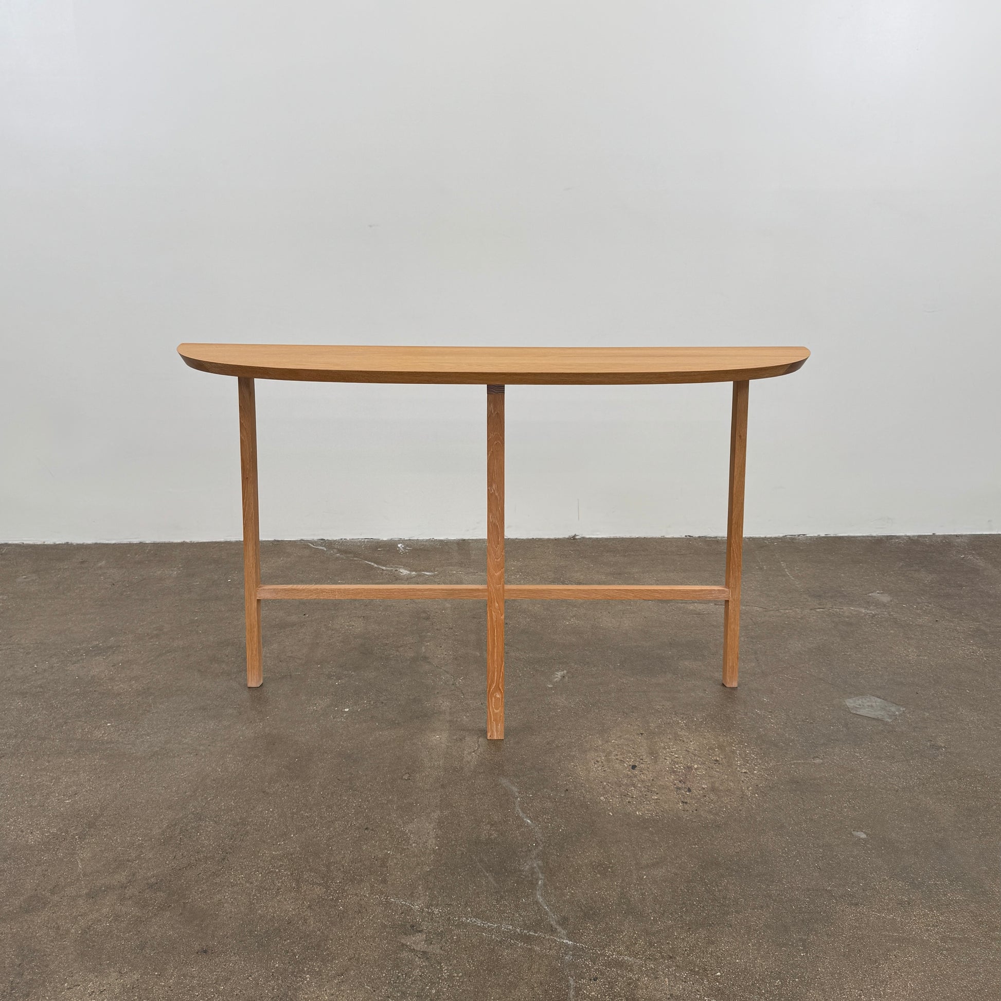 A De La Espada Trio Console Table 754CL by De La Espada stands against a white wall, showcasing modern woodworking with three vases, a beaded necklace, and a small stack of books arranged on its surface atop the concrete floor.