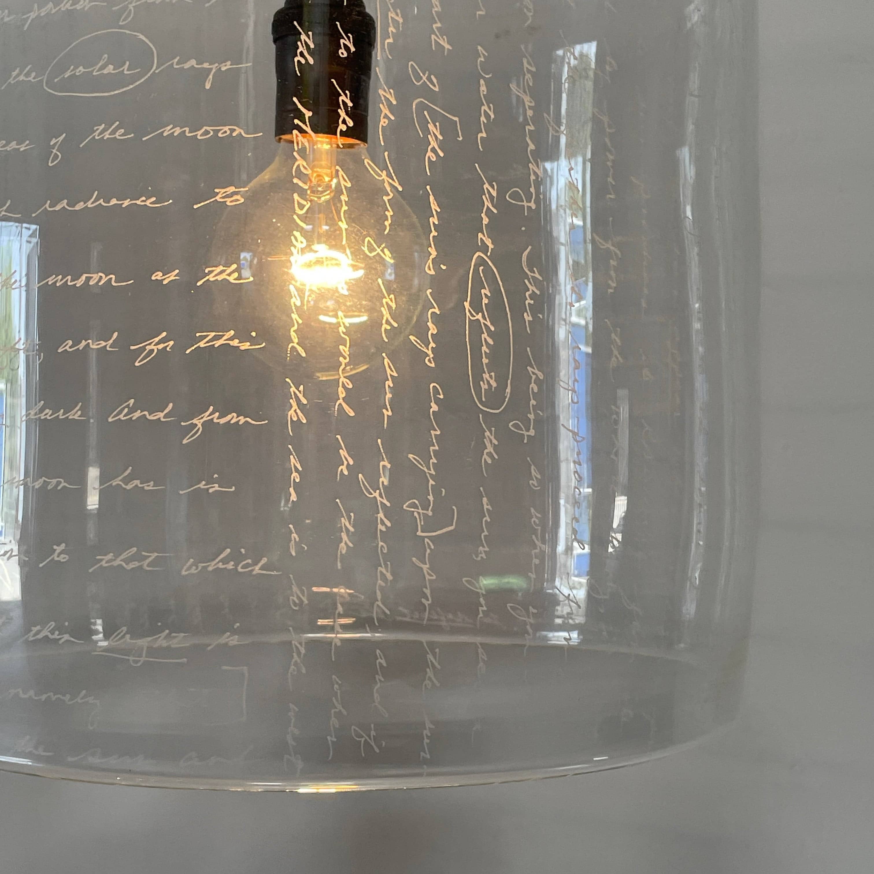 A unique functional art piece, this Alison Berger Word Pendant by Alison Berger showcases visible wires and mounting hardware against a white textured ceiling, reminiscent of Alison Berger's Word Pendant designs.