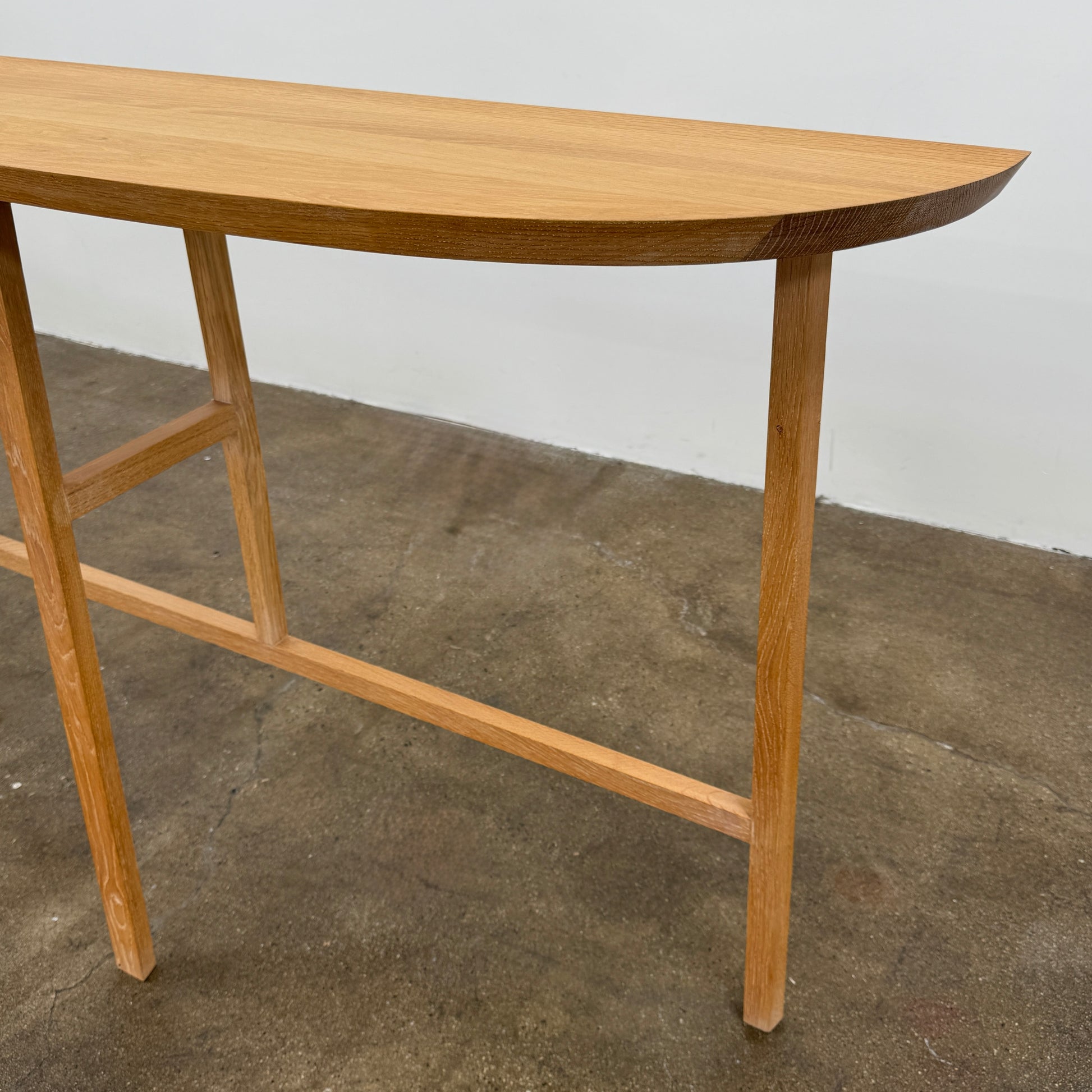 A De La Espada Trio Console Table 754CL by De La Espada stands against a white wall, showcasing modern woodworking with three vases, a beaded necklace, and a small stack of books arranged on its surface atop the concrete floor.