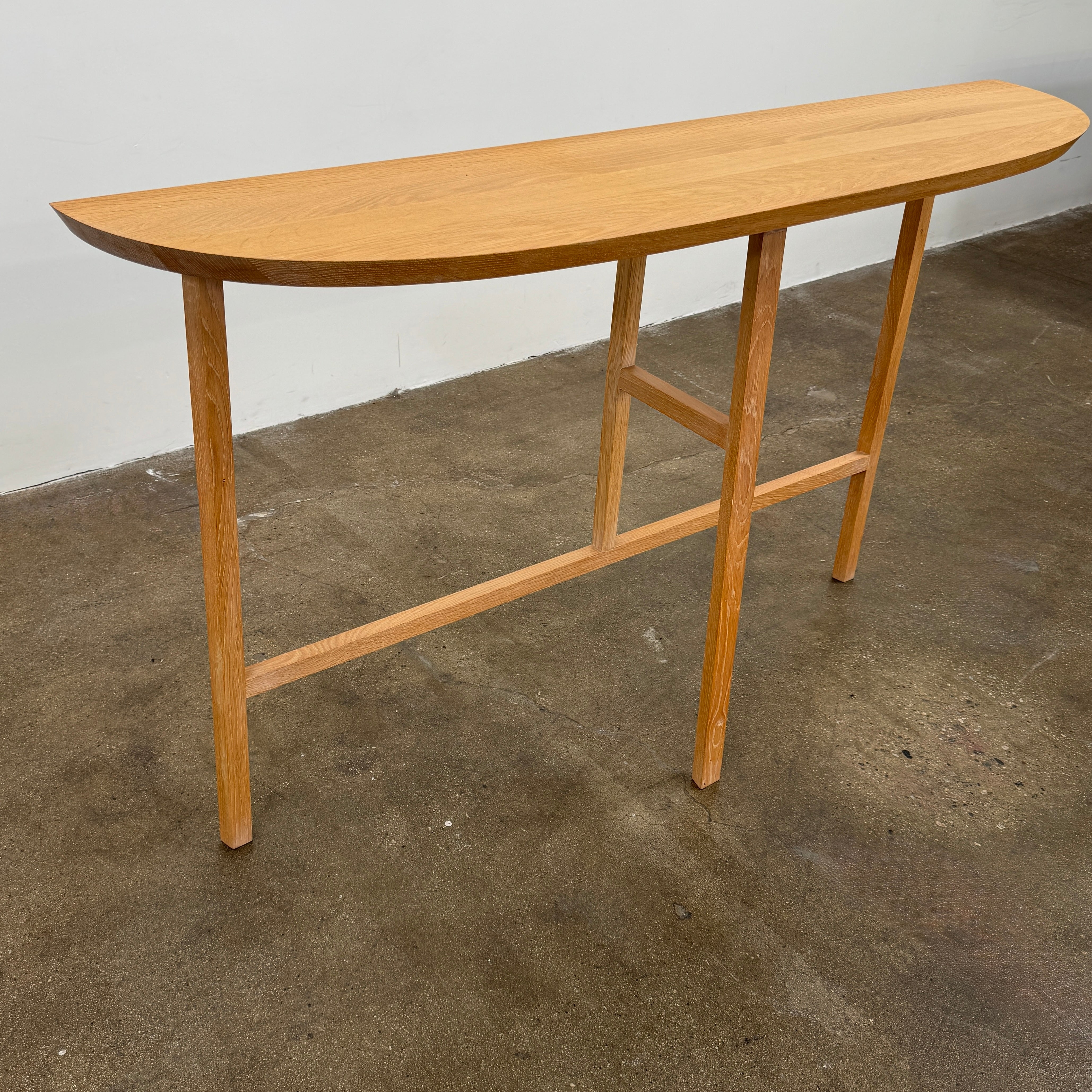A De La Espada Trio Console Table 754CL by De La Espada stands against a white wall, showcasing modern woodworking with three vases, a beaded necklace, and a small stack of books arranged on its surface atop the concrete floor.