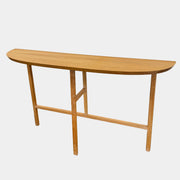 A De La Espada Trio Console Table 754CL by De La Espada stands against a white wall, showcasing modern woodworking with three vases, a beaded necklace, and a small stack of books arranged on its surface atop the concrete floor.