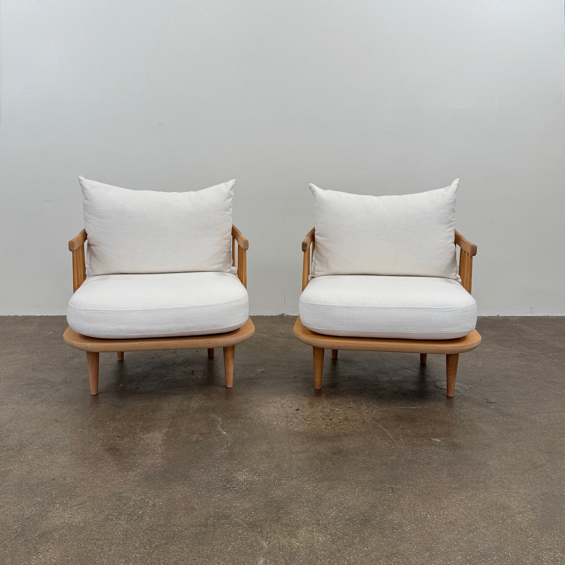 Two &Tradition FLY Lounge Chairs by Modern Resale, featuring white cushions, are arranged side by side on a bare concrete floor against a plain white wall, embodying Nordic minimalism for a refined modern interior.