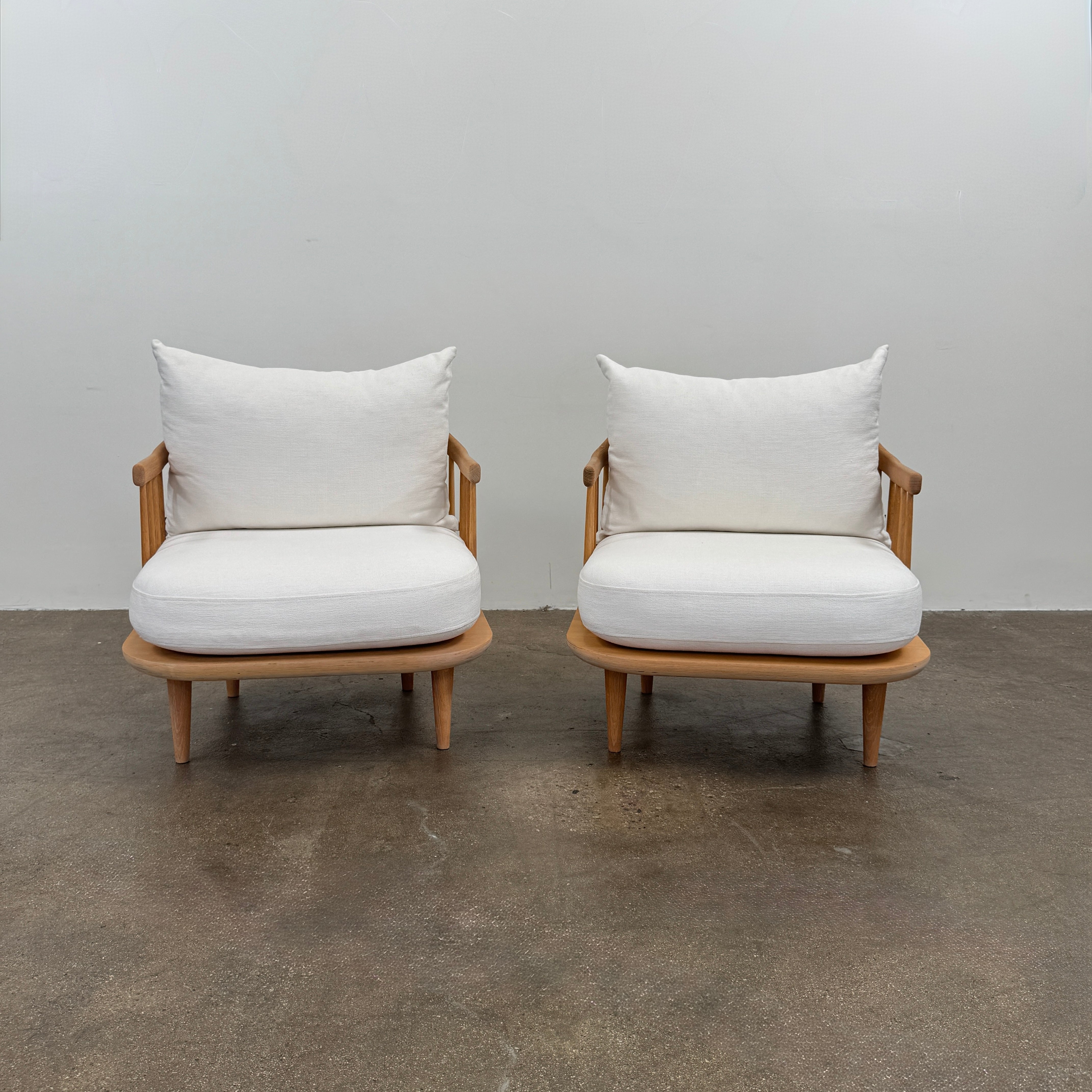 Two &Tradition FLY Lounge Chairs by Modern Resale, featuring white cushions, are arranged side by side on a bare concrete floor against a plain white wall, embodying Nordic minimalism for a refined modern interior.
