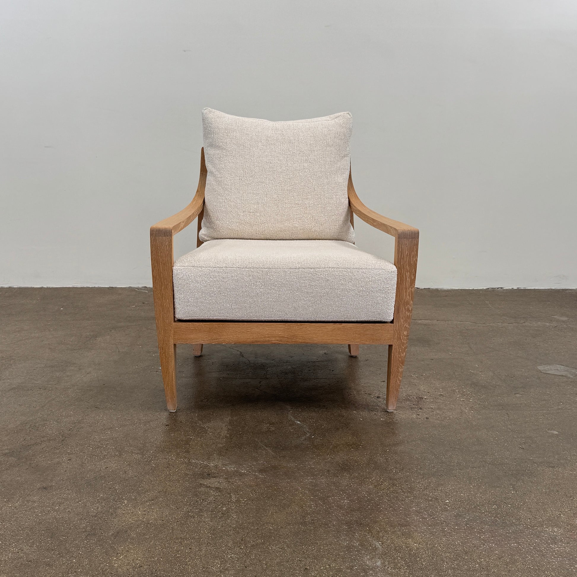 A De La Espada Low Lounge Chair 340 with light beige cushions is positioned on a polished concrete floor against a plain, light-colored wall.