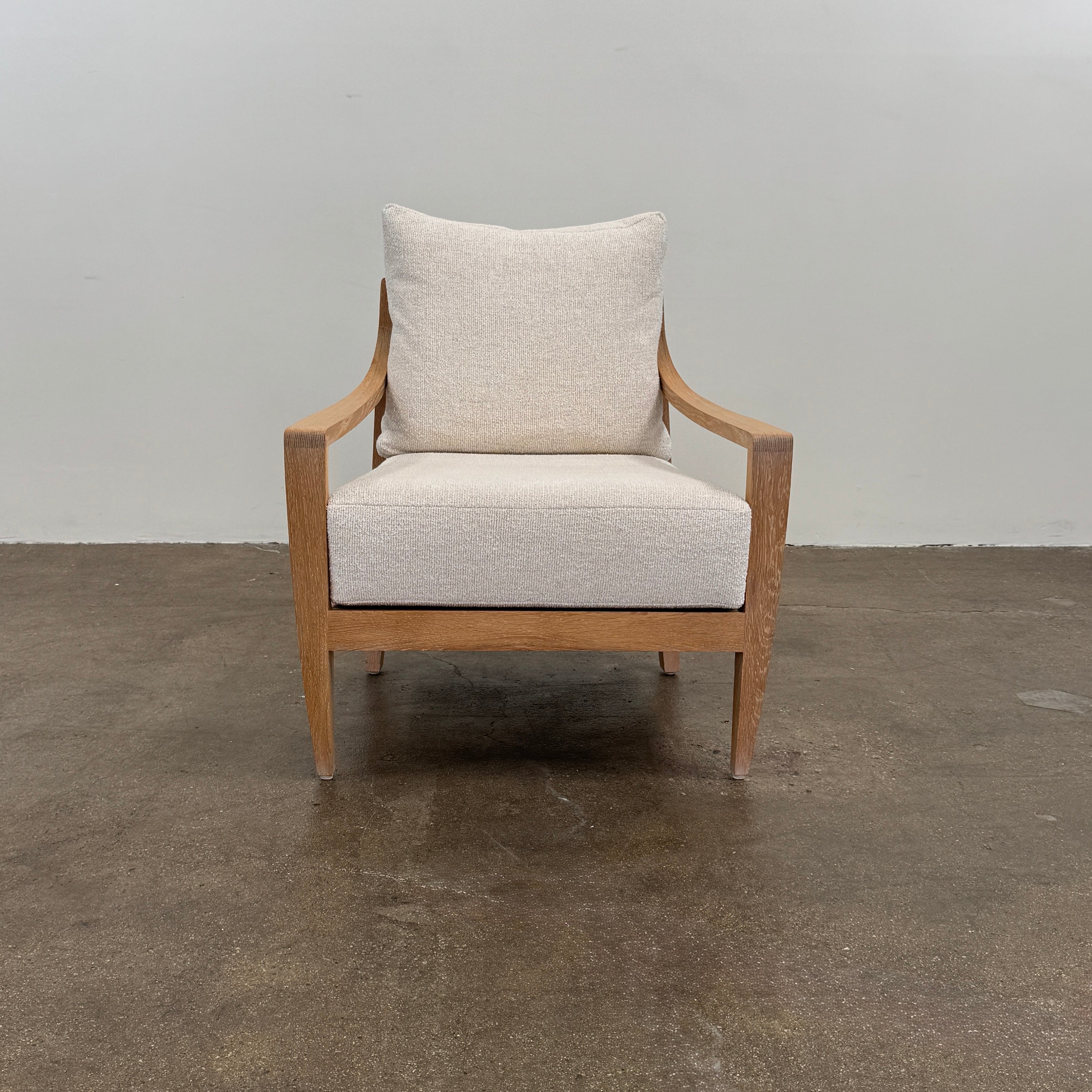 A De La Espada Low Lounge Chair 340 with light beige cushions is positioned on a polished concrete floor against a plain, light-colored wall.