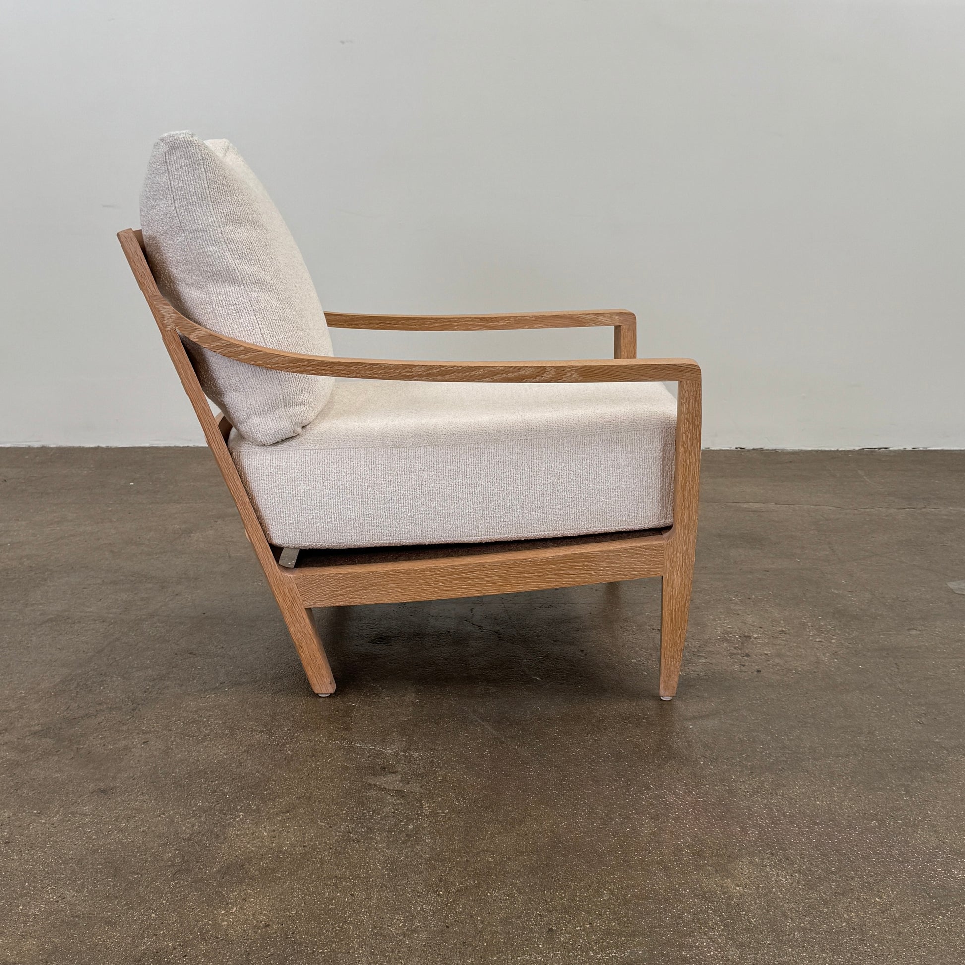 A De La Espada Low Lounge Chair 340 with light beige cushions is positioned on a polished concrete floor against a plain, light-colored wall.