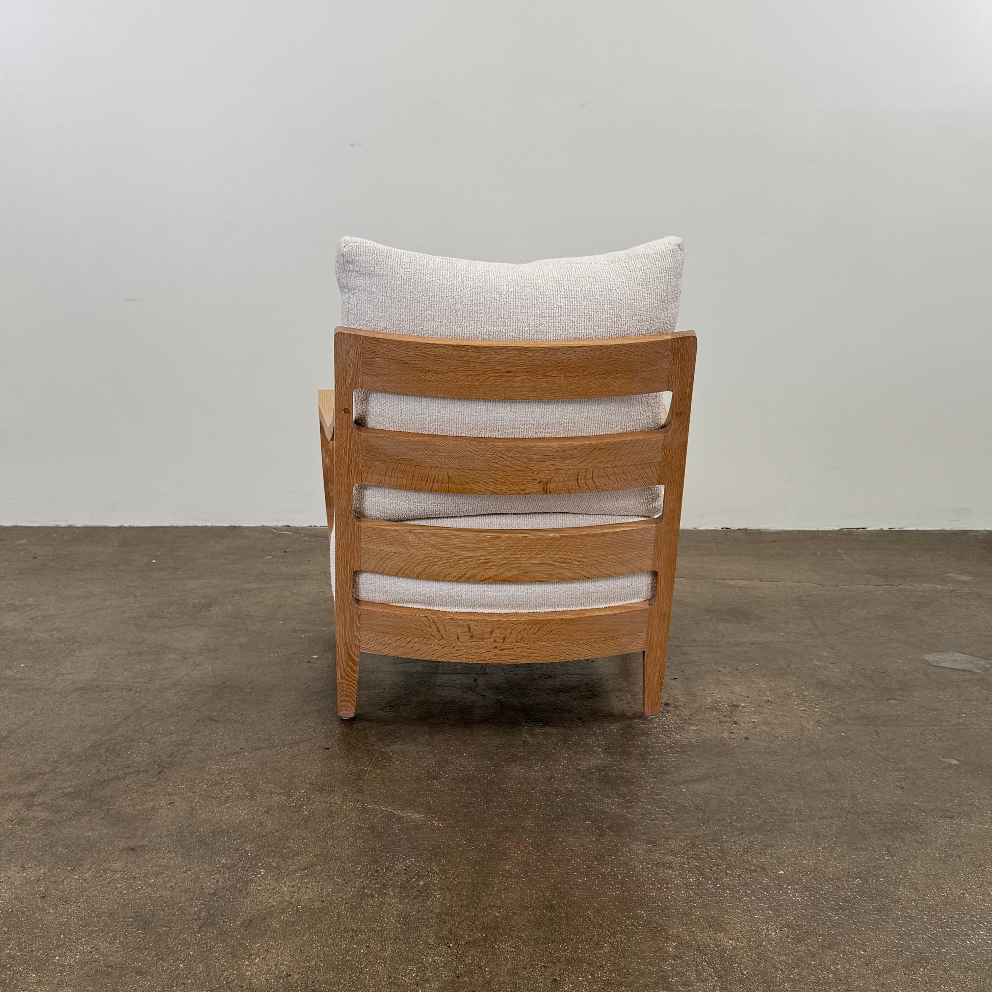 A De La Espada Low Lounge Chair 340 with light beige cushions is positioned on a polished concrete floor against a plain, light-colored wall.