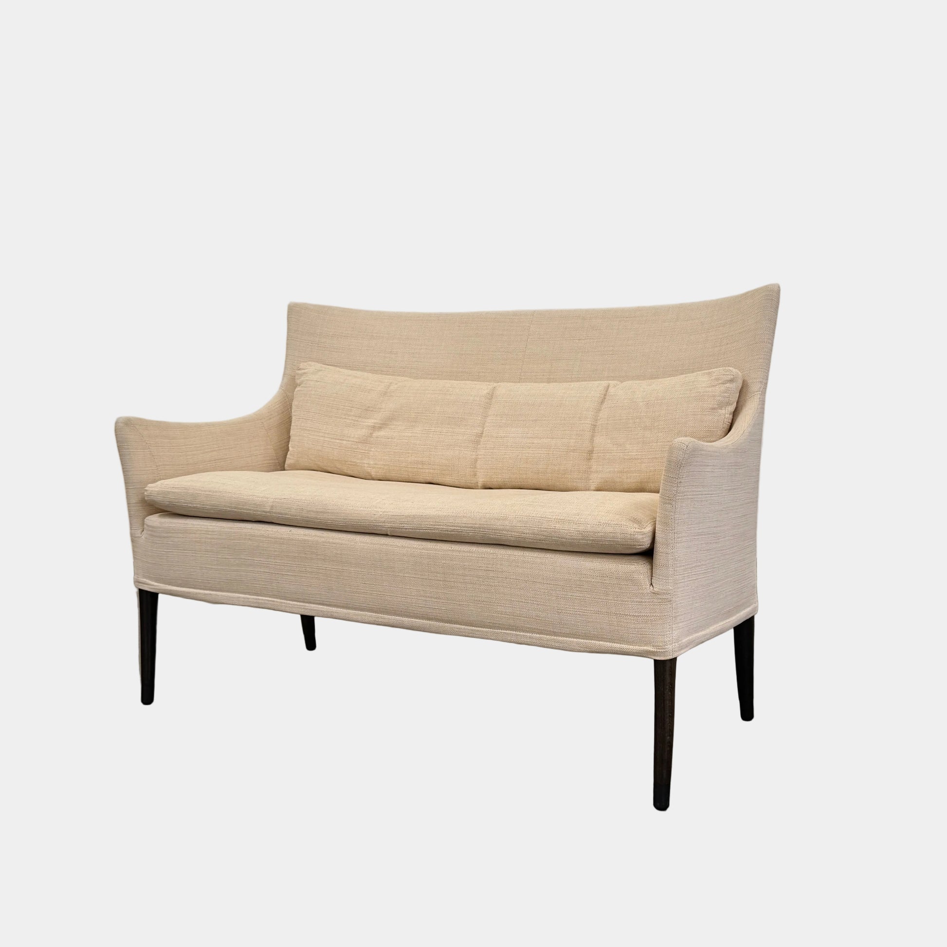 A Vintage Giorgetti Settee by Giorgetti, upholstered in beige with two matching cushions, black legs, and a high back, is placed on a polished concrete floor against a plain white wall.