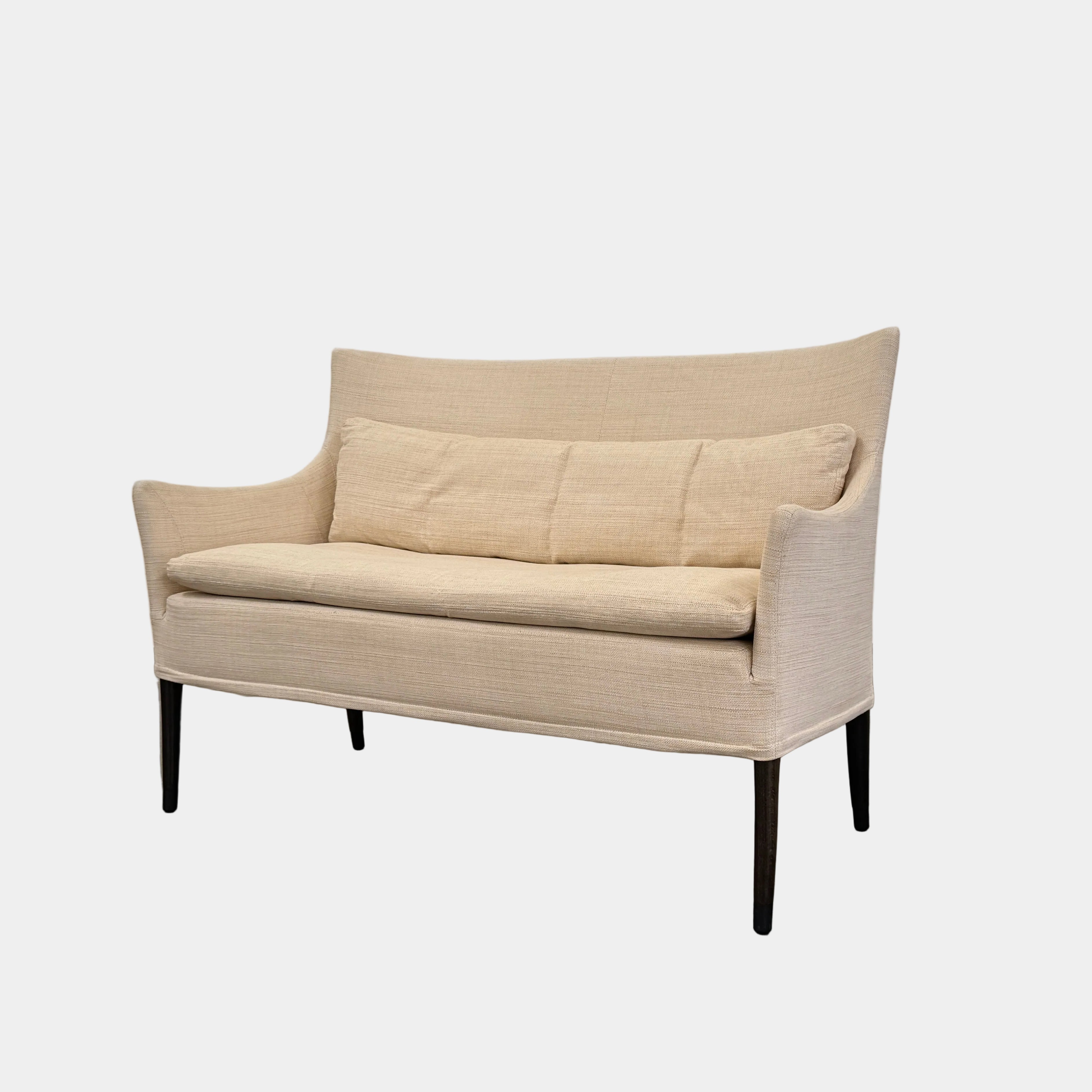 A Vintage Giorgetti Settee by Giorgetti, upholstered in beige with two matching cushions, black legs, and a high back, is placed on a polished concrete floor against a plain white wall.