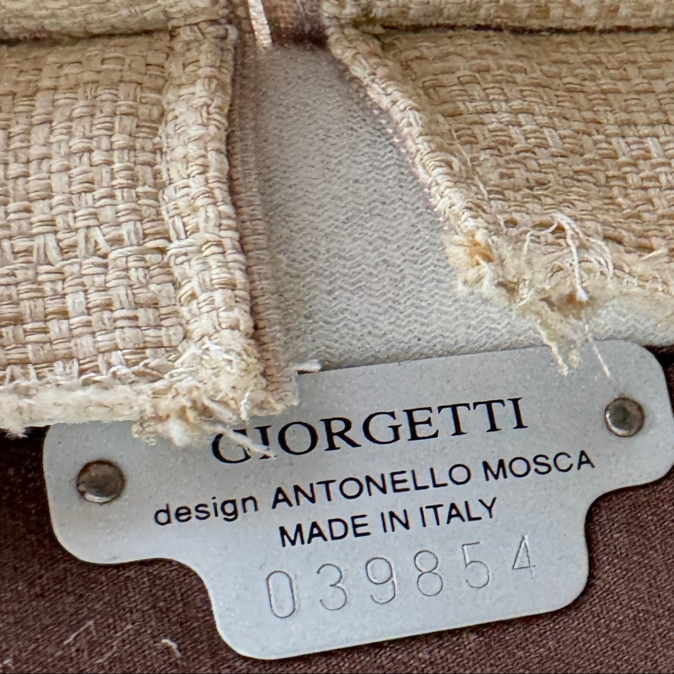 A Vintage Giorgetti Settee by Giorgetti, upholstered in beige with two matching cushions, black legs, and a high back, is placed on a polished concrete floor against a plain white wall.