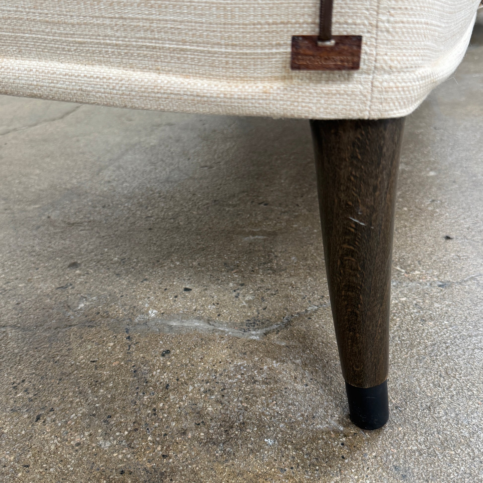 A Vintage Giorgetti Settee by Giorgetti, upholstered in beige with two matching cushions, black legs, and a high back, is placed on a polished concrete floor against a plain white wall.
