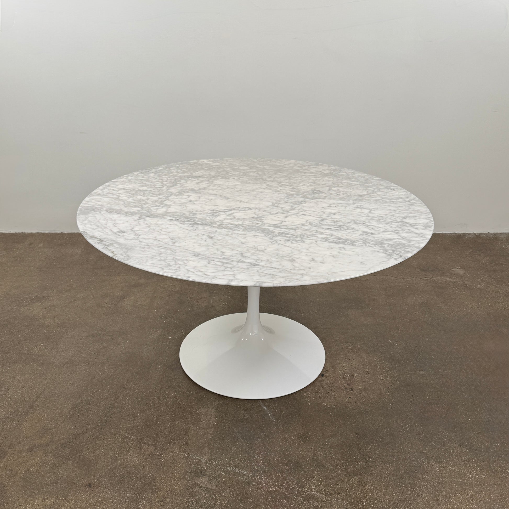 The Knoll Saarinen Table 54″ Round Arabescato Marble, designed by Knoll and inspired by the iconic Saarinen silhouette, features a single central pedestal base and is crafted from luxurious Arabescato marble. It is photographed against a plain white background.