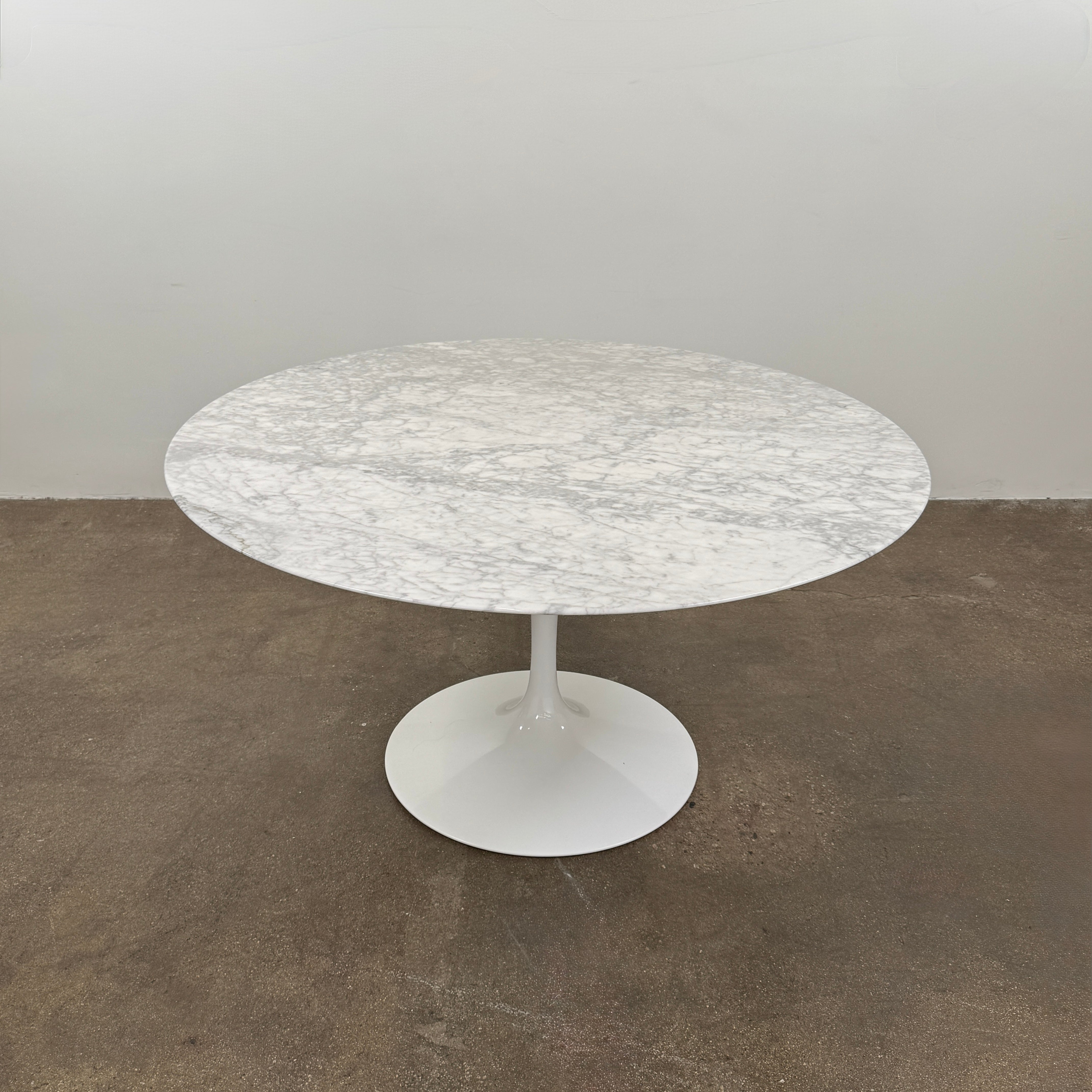 The Knoll Saarinen Table 54″ Round Arabescato Marble, designed by Knoll and inspired by the iconic Saarinen silhouette, features a single central pedestal base and is crafted from luxurious Arabescato marble. It is photographed against a plain white background.
